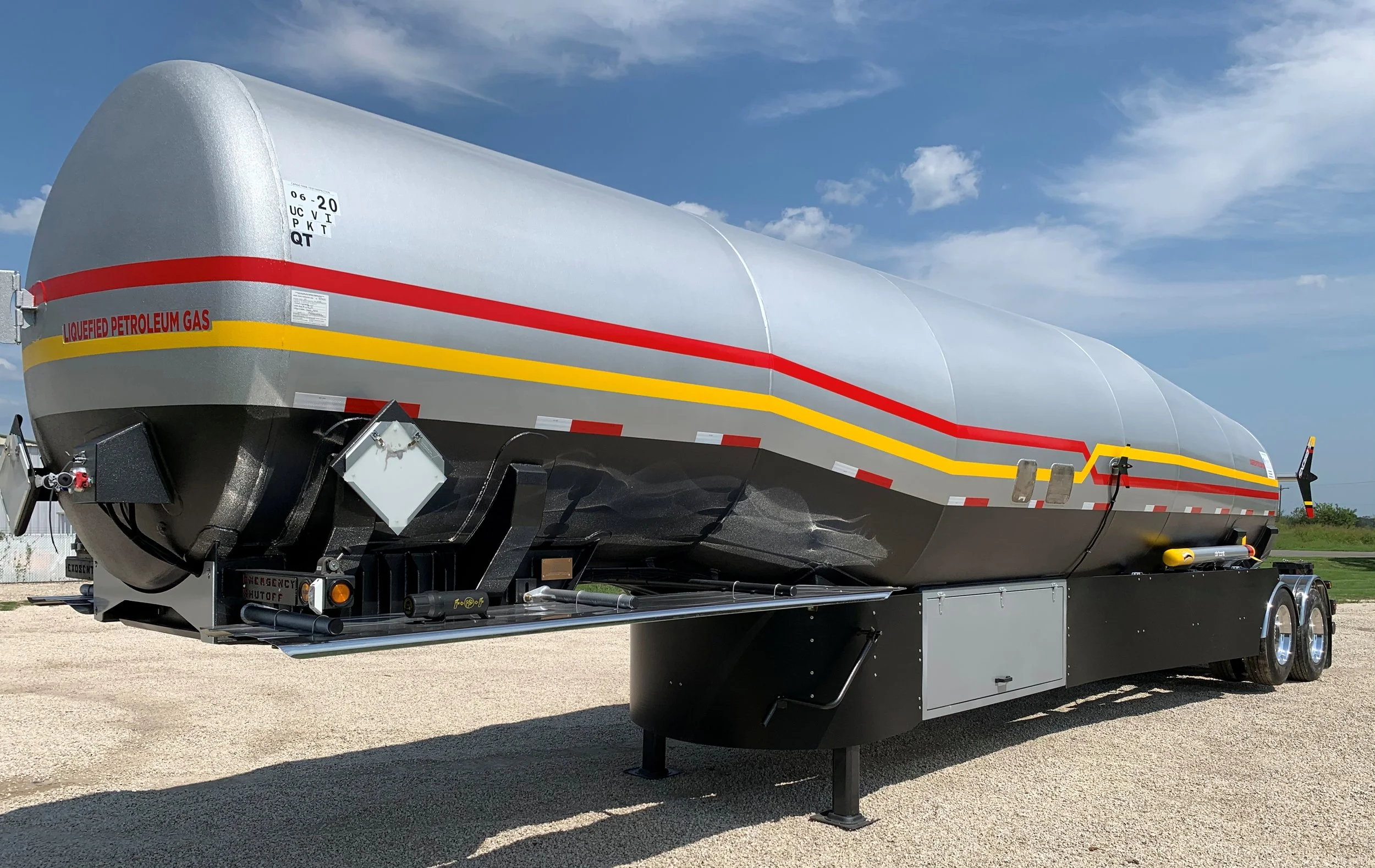 Large fuel tanker trailer labeled for carrying liquefied petroleum gas, painted gray with red and yellow stripes, parked outdoors under a blue sky.