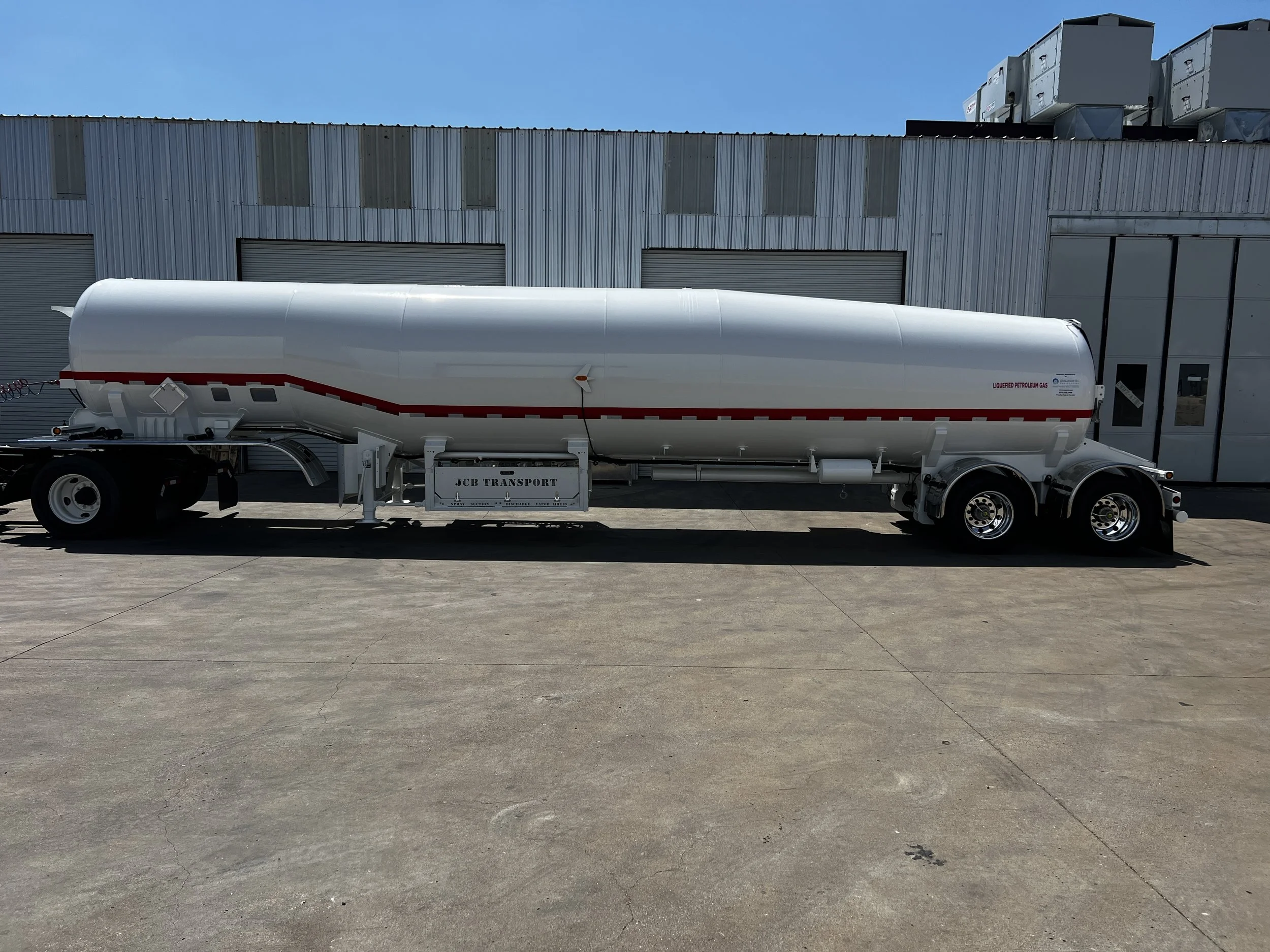 White fuel tanker truck parked outside a building with metal siding.