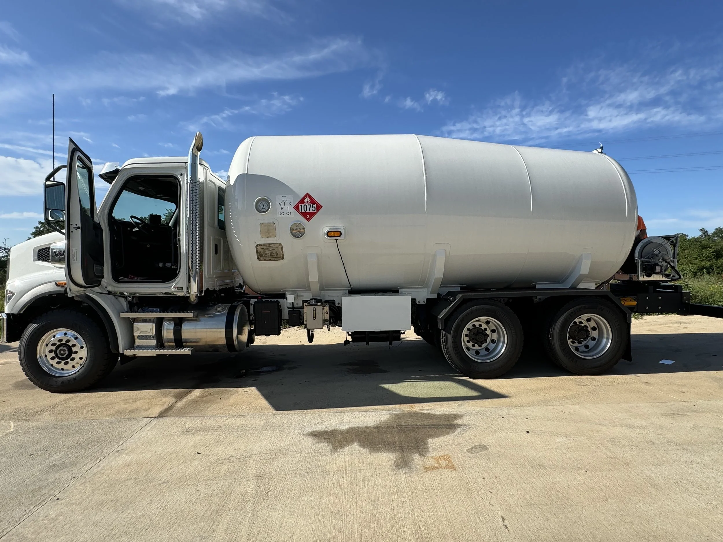 White tanker truck parked on pavement under blue sky with wispy clouds.
