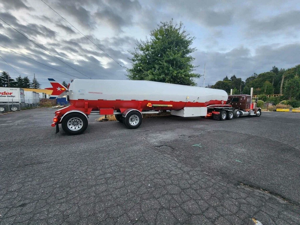 A semi-truck with a red and white tanker trailer parked on an asphalt lot under cloudy skies.