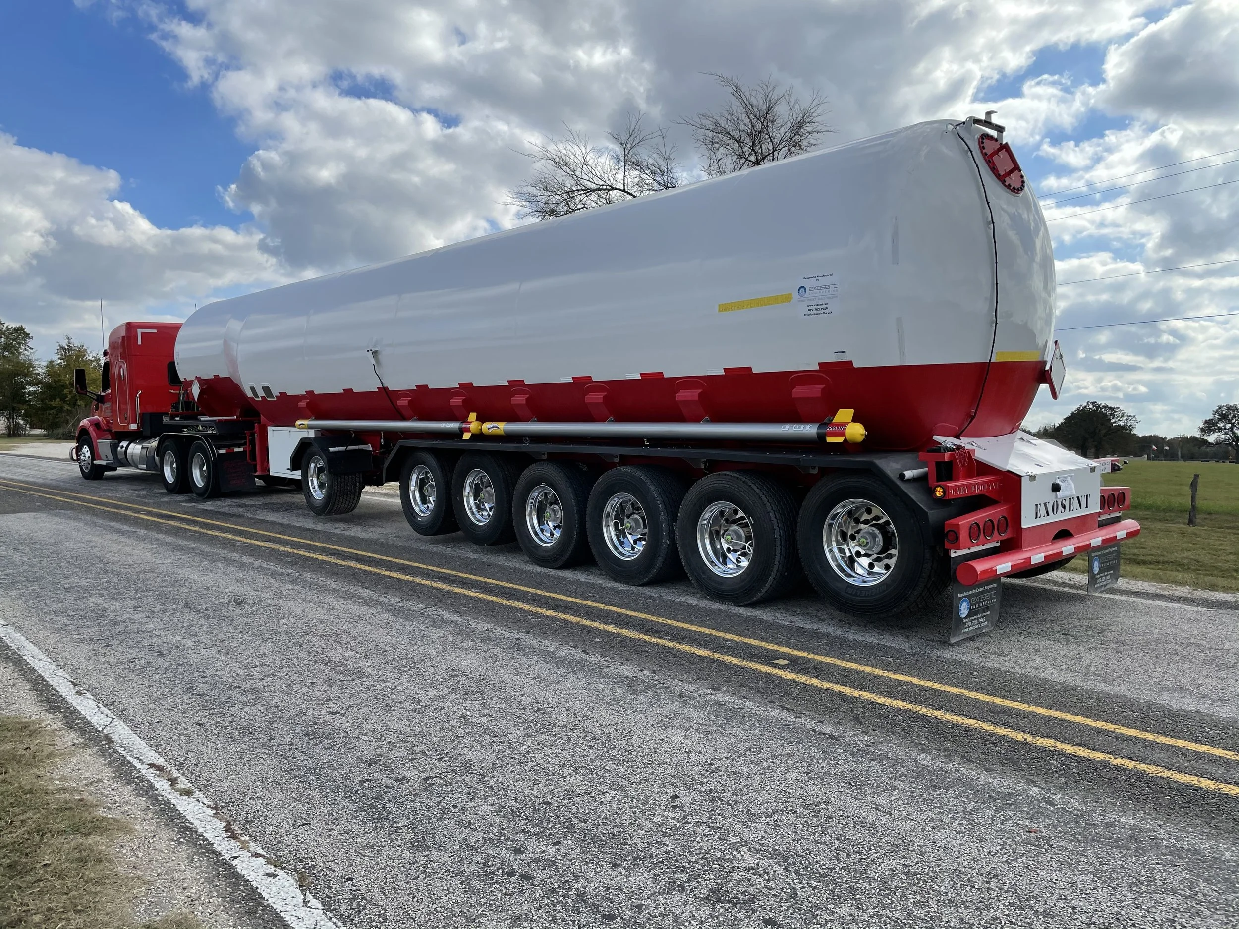 Large white and red tanker truck parked on the side of a rural road under a partly cloudy sky.
