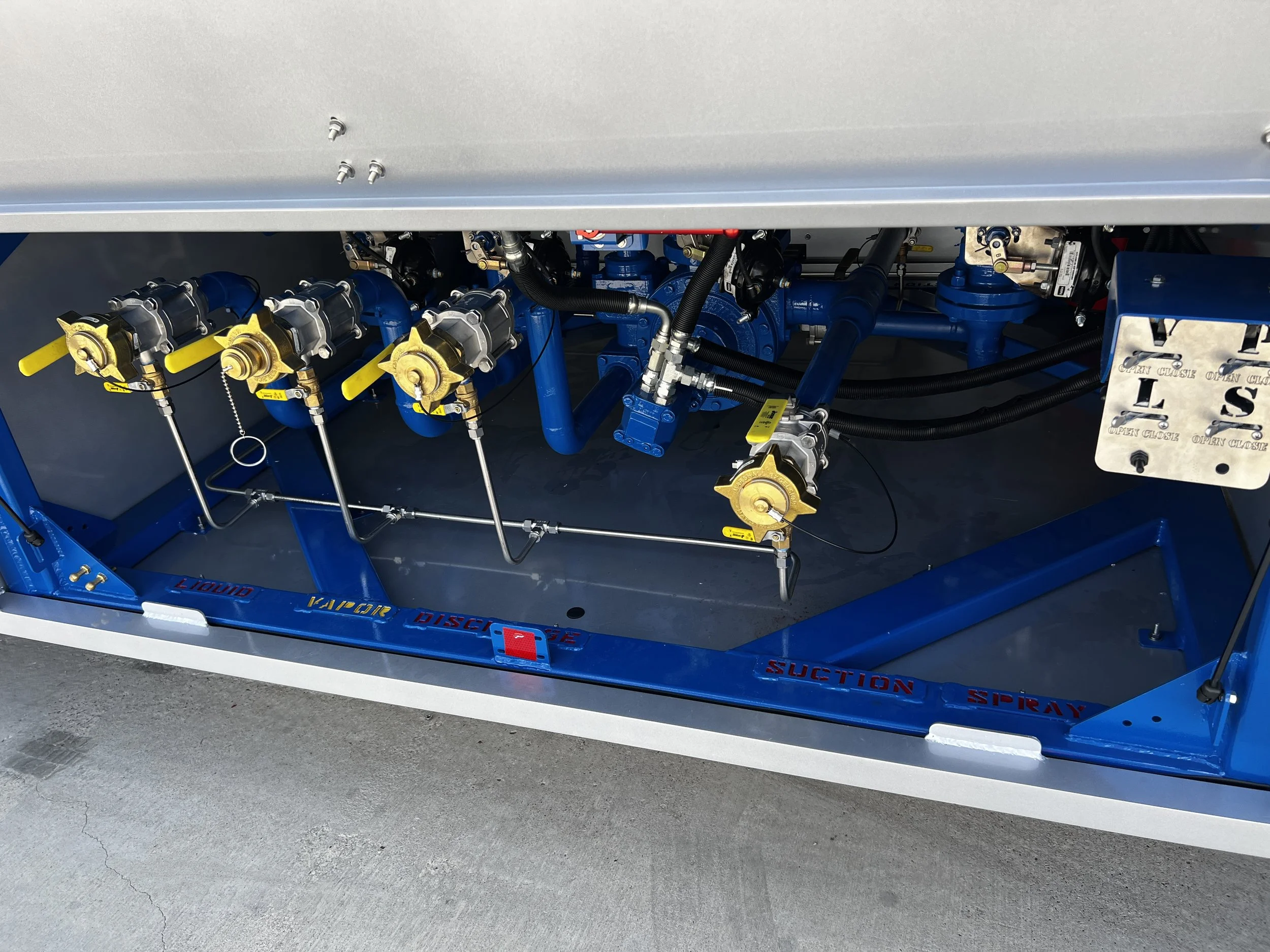 Inside a machine with blue and metallic components, including valves, pipes, and labels indicating functions like liquid, vapor, suction, discharge, and spray.