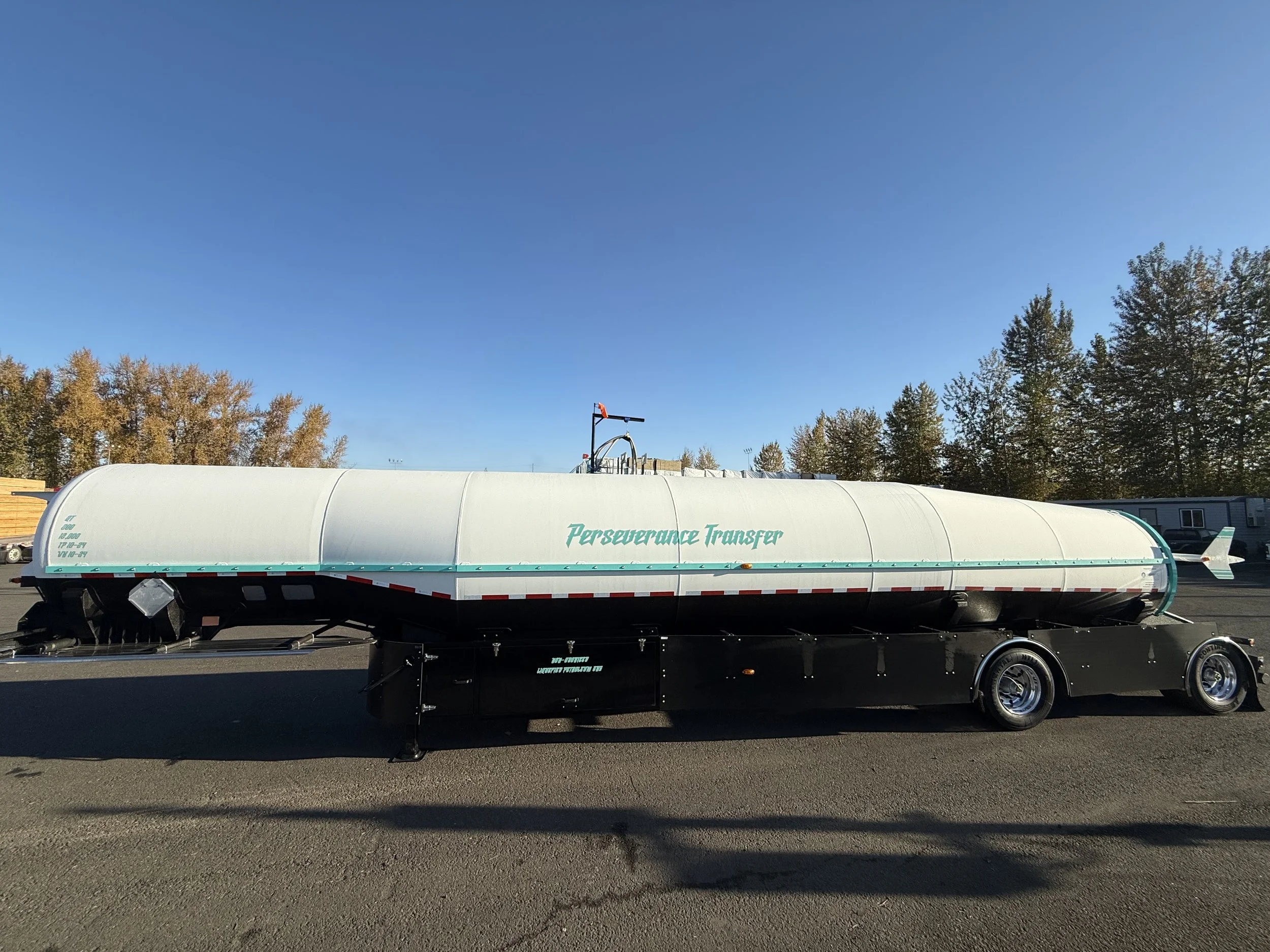 A rocket-shaped vehicle on a trailer with the words 'Perseverance Transfer' painted on the side, parked outdoors under a clear blue sky with trees in the background.