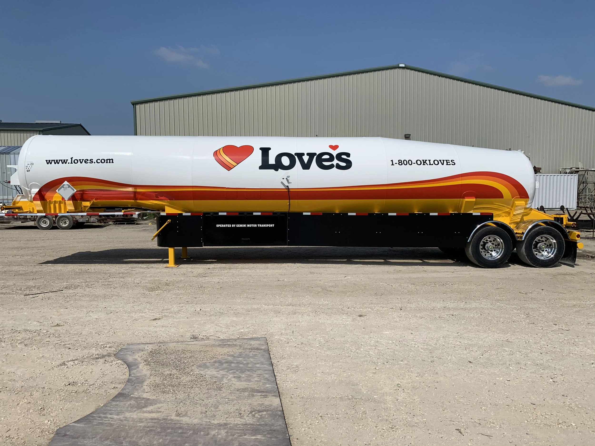 A large Love's truck fuel tank trailer parked outdoors on a dirt lot with a beige industrial building in the background.