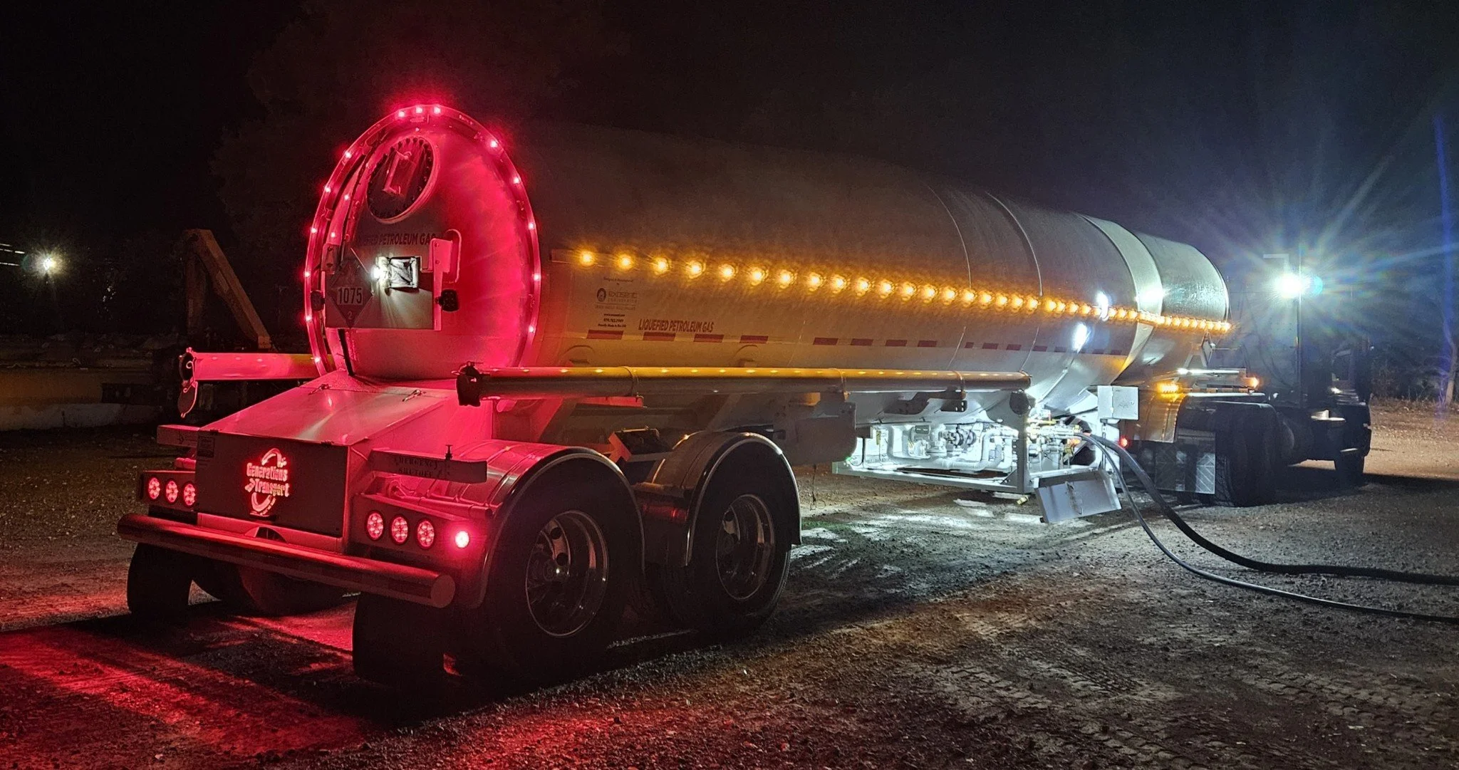 A tanker truck filled with liquefied petroleum gas is illuminated at night, showing bright red and white lights.