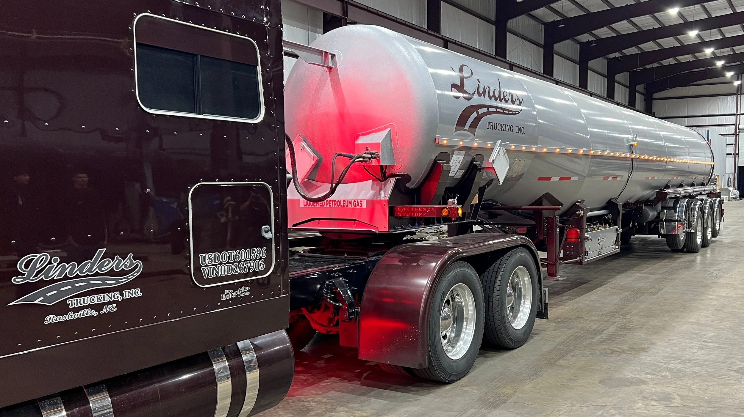 A large tanker truck inside a warehouse with the logo 'Linders Trucking, Inc.' on the side. The tanker is silver, and the truck cab is dark red. The tanker has caution labels for petroleum gas.