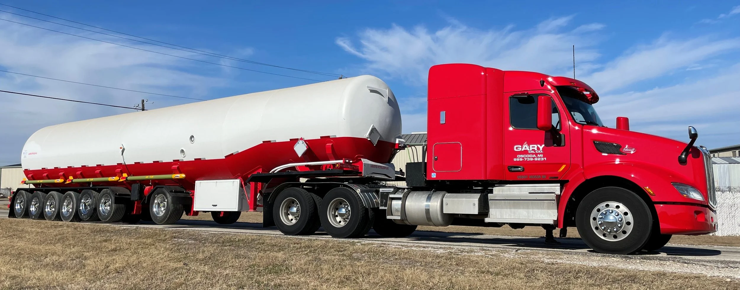 Red tanker truck parked outdoors under a blue sky with some clouds.