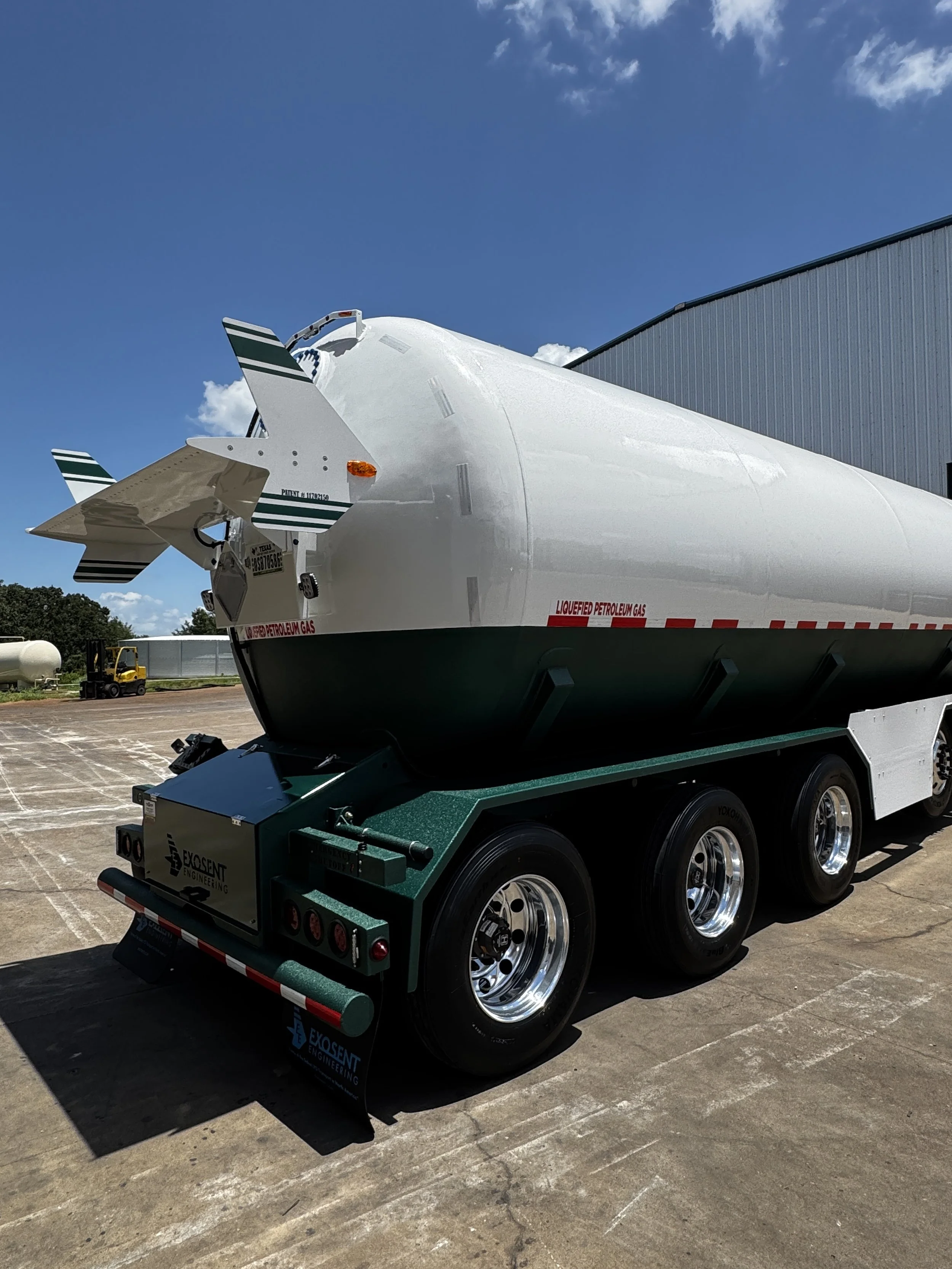 A large white liquid fuel tanker truck parked outdoors on a concrete lot under a blue sky with clouds. The trailer has green and black markings with the words "LIQUEFIED PETROLEUM GAS" written on the side. The truck's chassis has a green base with mu