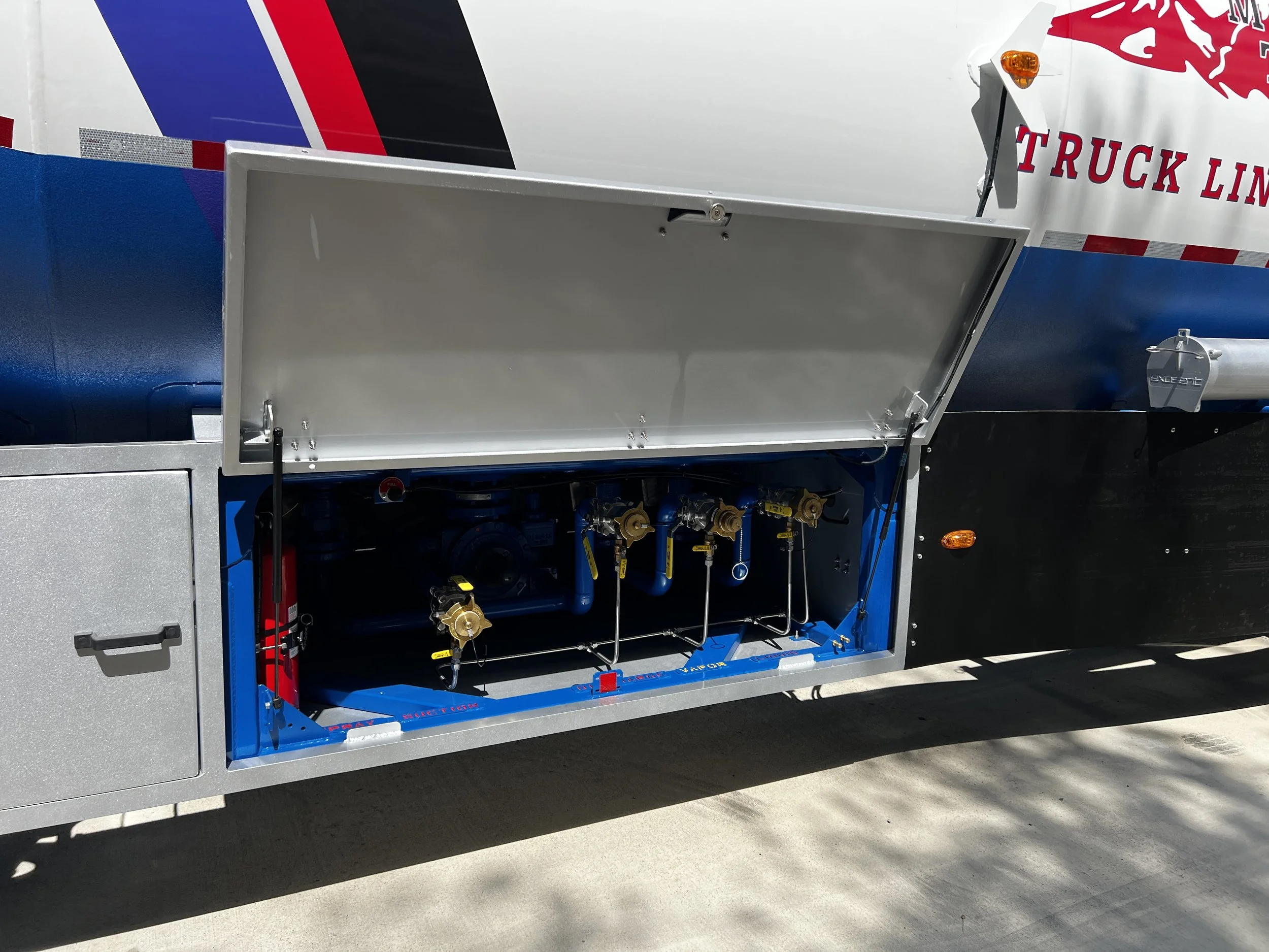 Side of a semi-truck with an open panel revealing mechanical components and pipelines inside.
