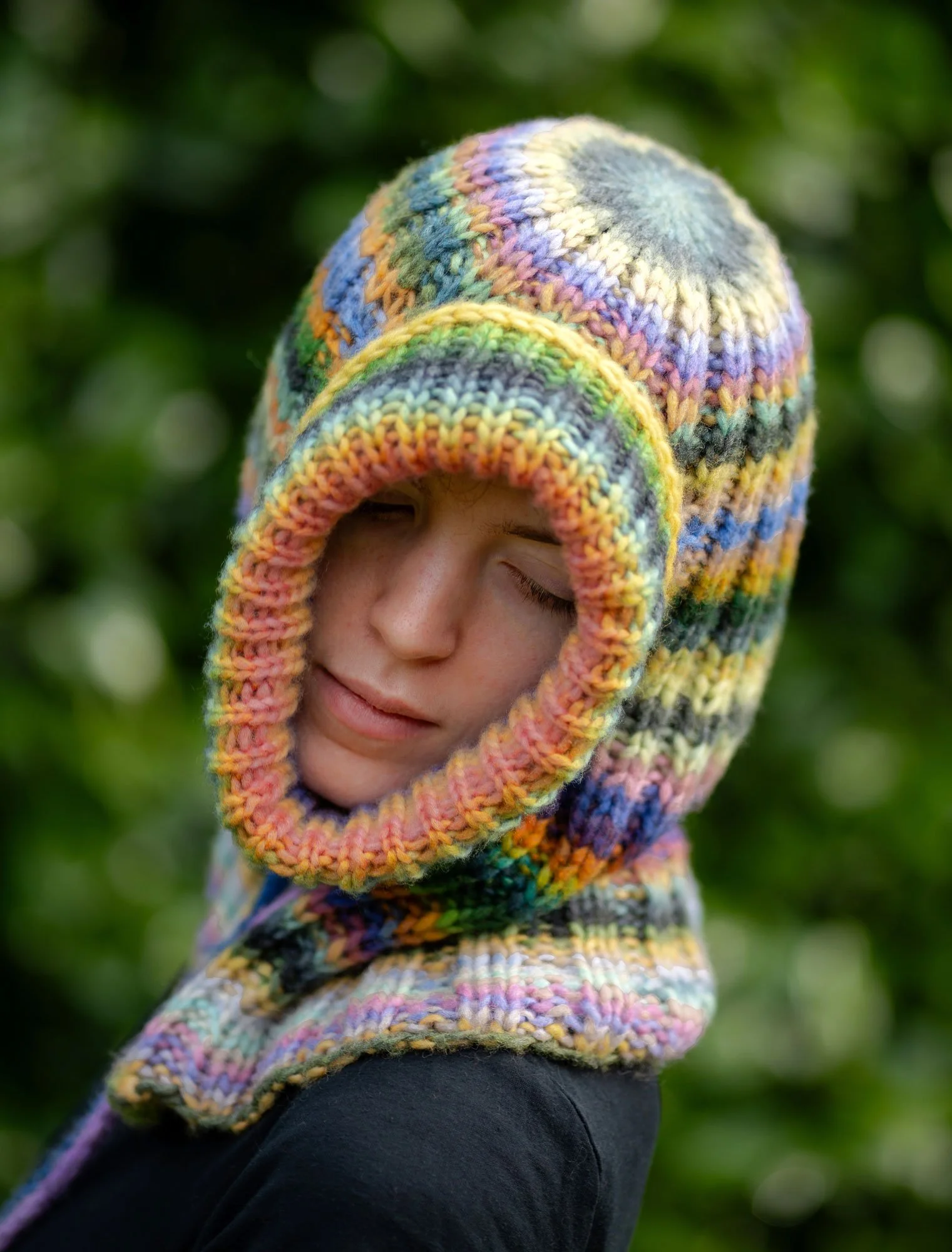 Person wearing a colorful, knitted hood with eye closed