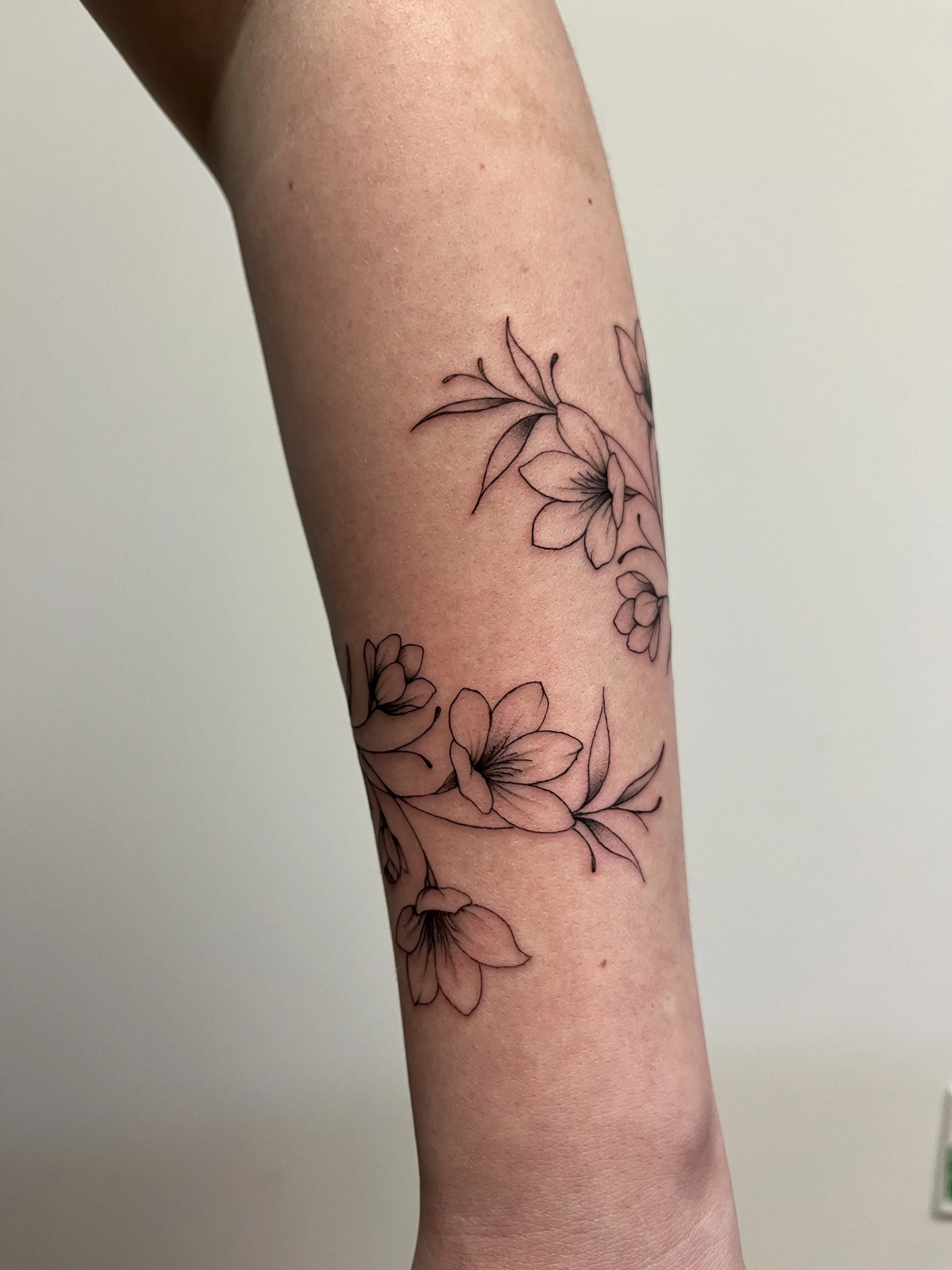 custom floral wrap fine line tattoo on females lower forearm