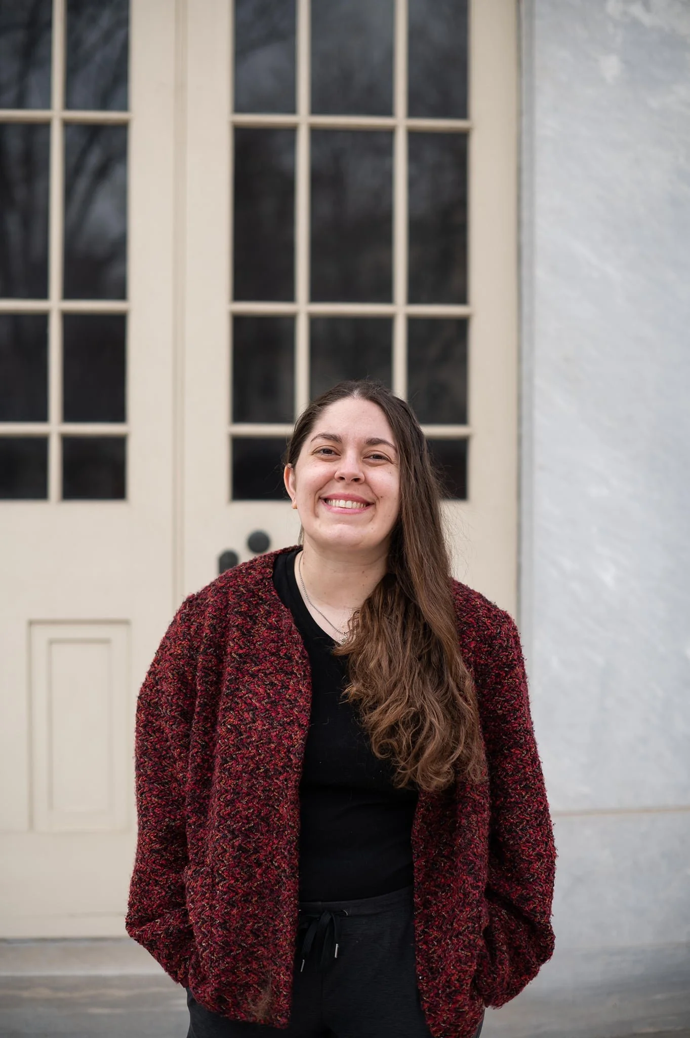 Sarah DeGeorge stands in front of building with a red cardigan on