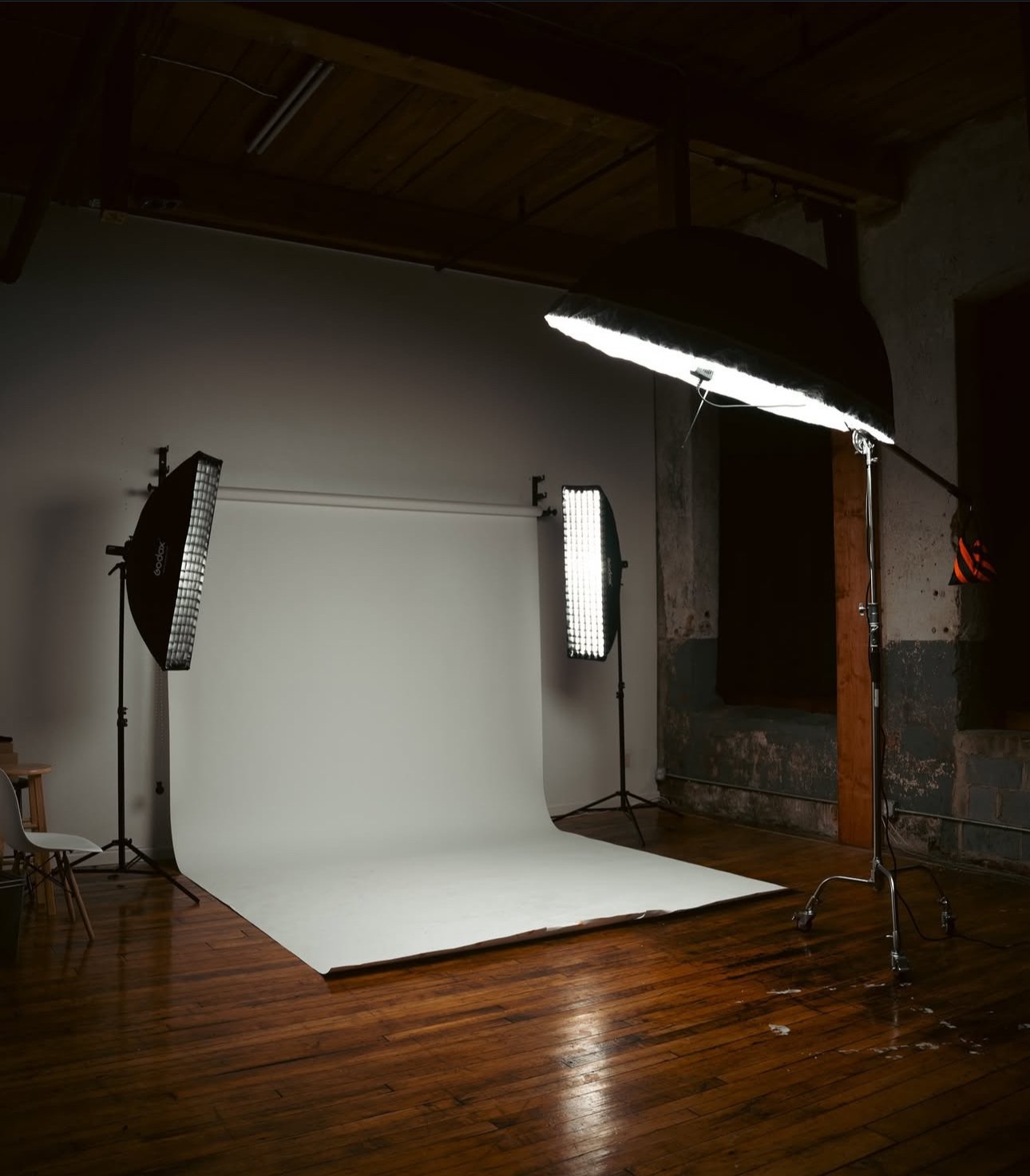 Empty photography studio with a white backdrop, studio lights, and wooden floors.