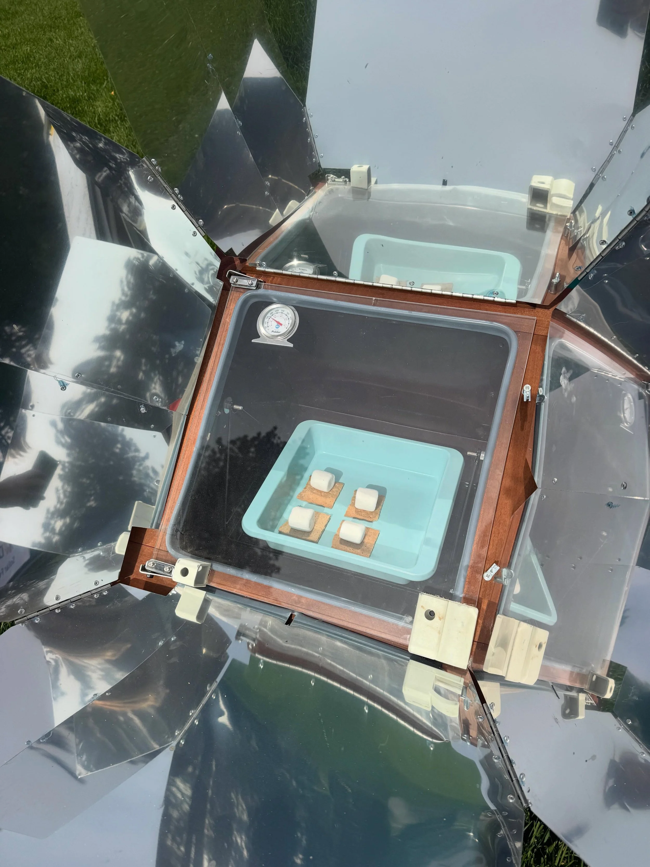 What is going on here?! This is a solar over which uses reflective panels to direct extra sunlight into the dark oven box! When paired with the clear window, all the heat conducted by the mirrors becomes trapped and heats up &mdash;- acting like a gr