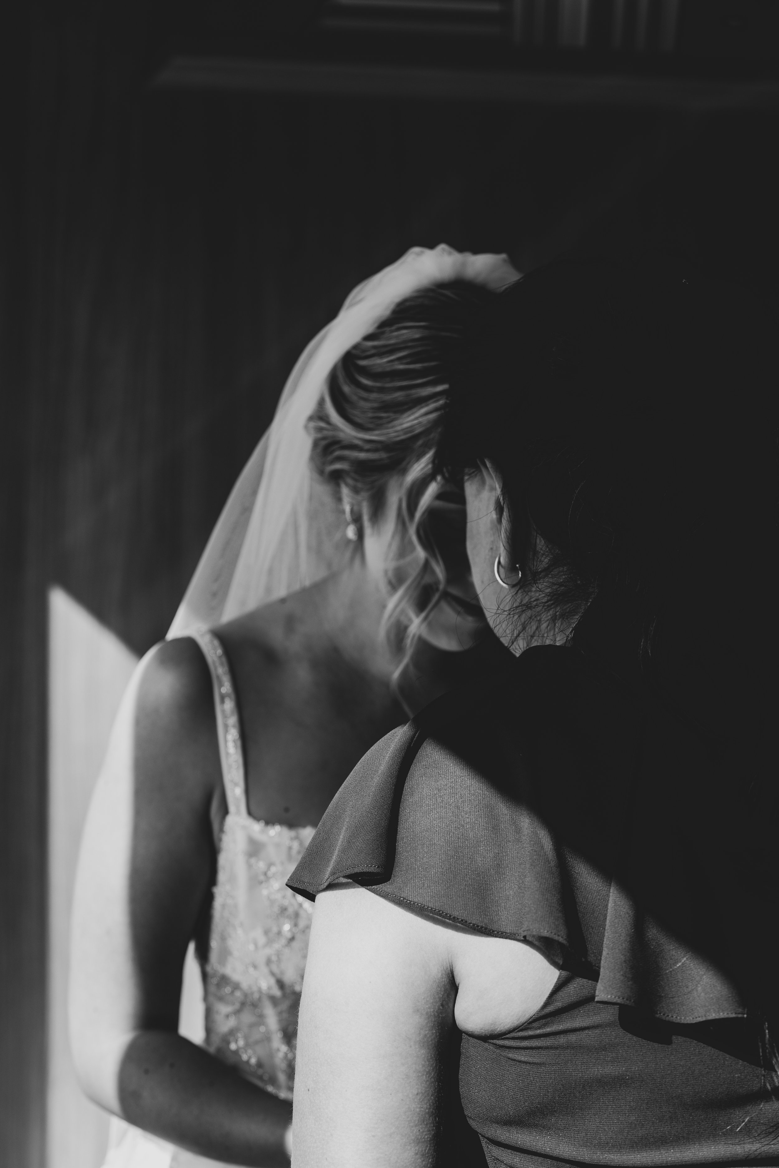 Black and white photo of a bride and another woman in an intimate moment, capturing emotion and detail in the bride's dress and veil.