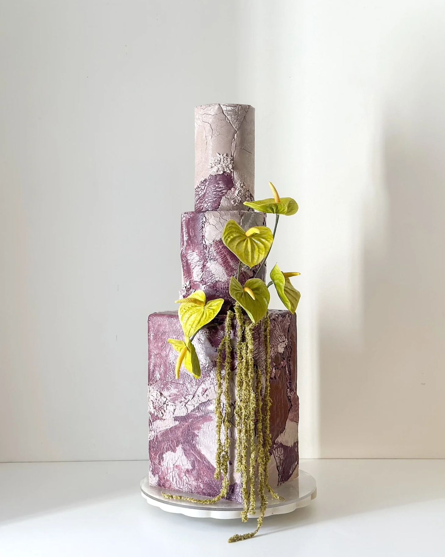 luxury wedding cake, San Diego wedding cake, wedding cake, cake art, Southern California wedding cake. Luxury fine art wedding cake showcasing dramatic burgundy marbled stone textures and a vibrant, lifelike branch of climbing green anthurium and cas