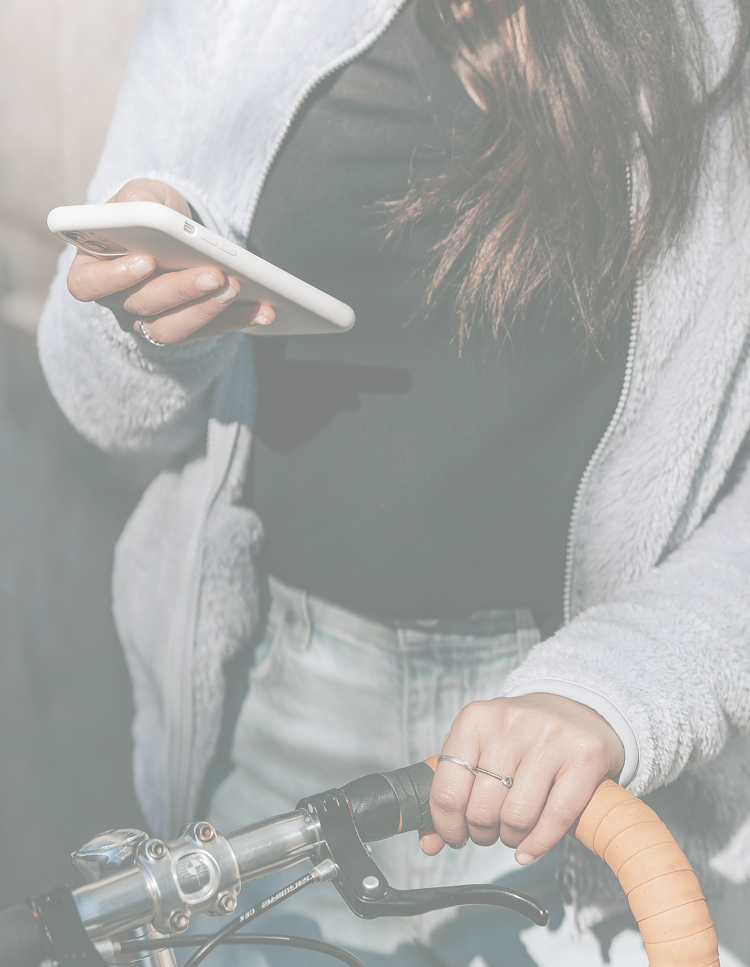 A woman holding a smartphone in one hand and gripping the handlebar of a bicycle with the other hand.