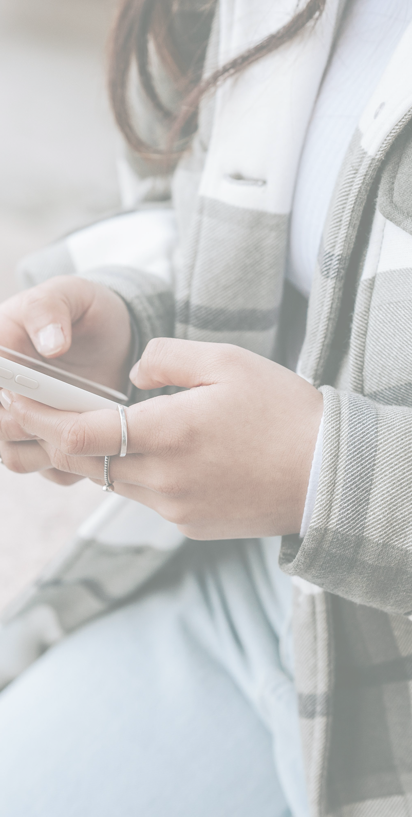 Close-up of a person wearing a grey and white plaid jacket, holding a smartphone with both hands, with a silver ring on their ring finger and painted nails.