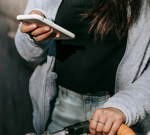 A person wearing a black shirt and gray hoodie holding a smartphone in one hand and a bicycle handlebar in the other.