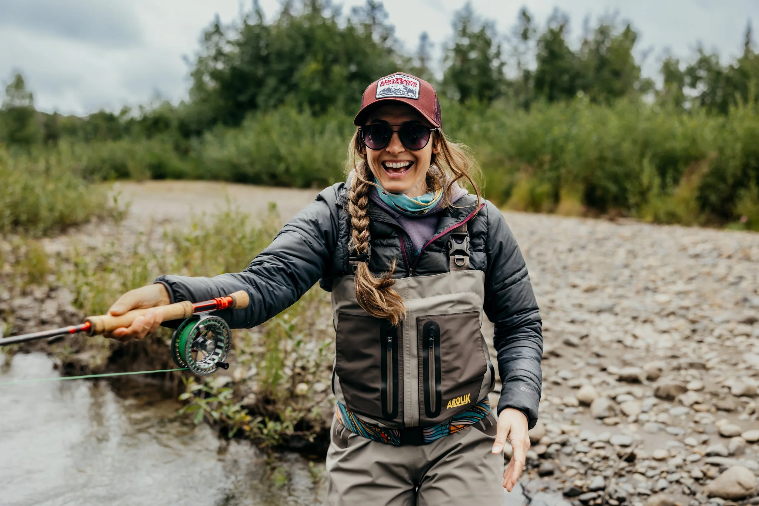 Woman fly fishing in a rocky Alaska river wearing Arolik fishing waders and outdoor gear.