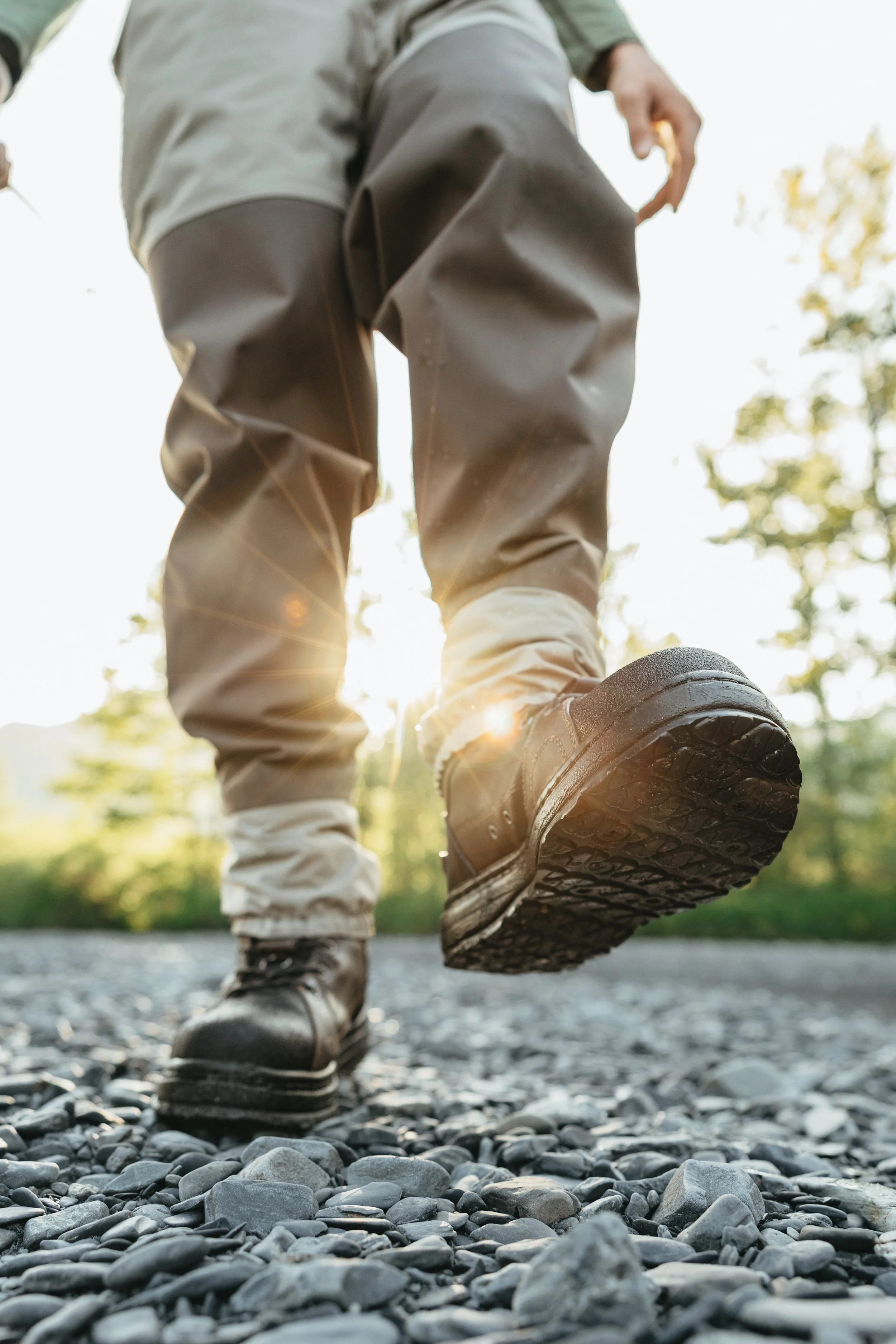 Close-up of waterproof fishing boots stepping through rocky river terrain, showing traction and durability in outdoor conditions.