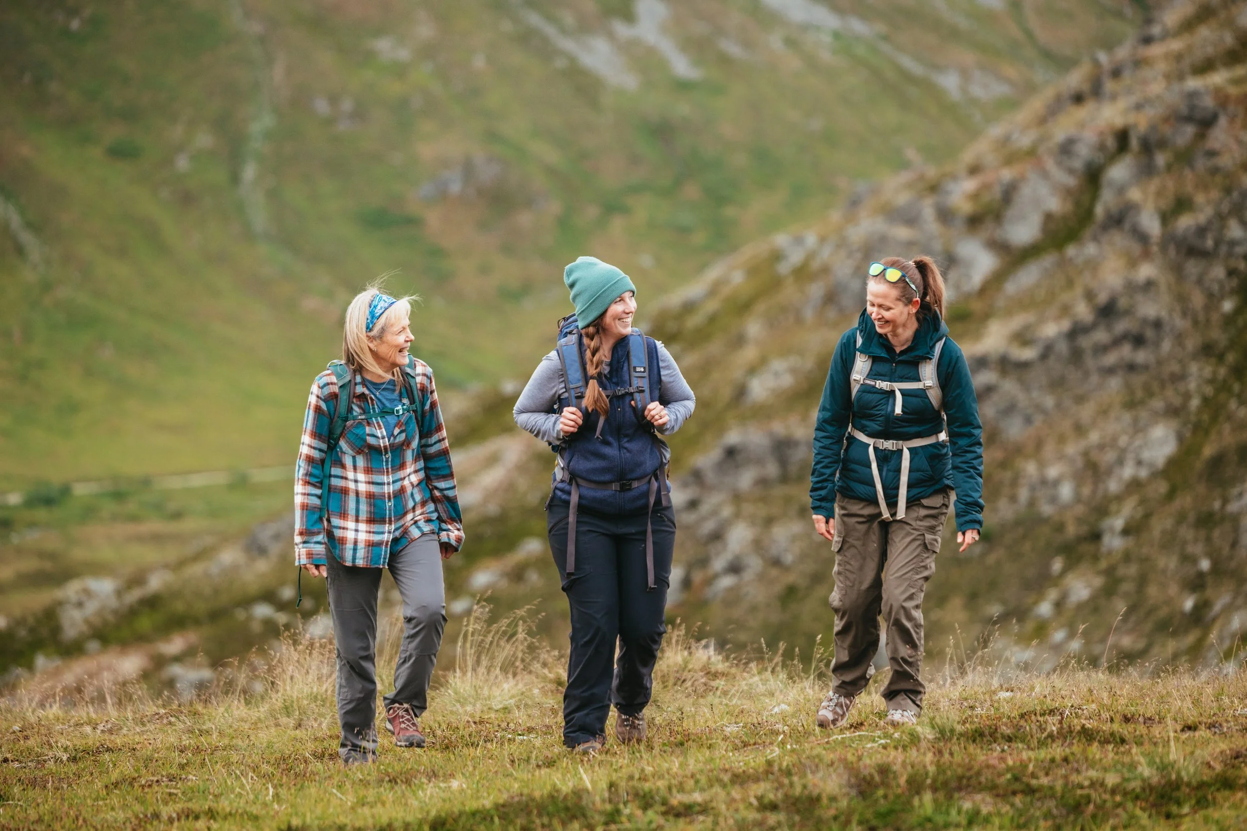 Three women laugh while hiking and trekking through the Alaska mountains.