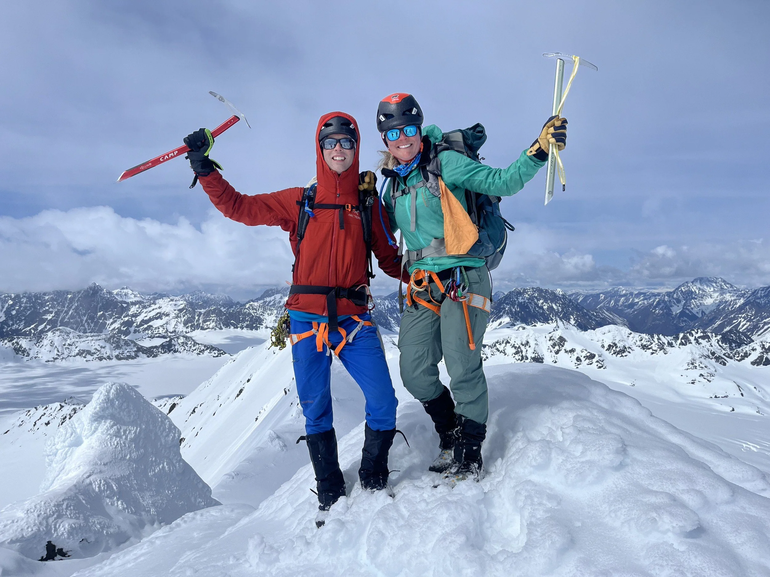 Two mountain climbers cheer with their hands up as they summit a mountain.
