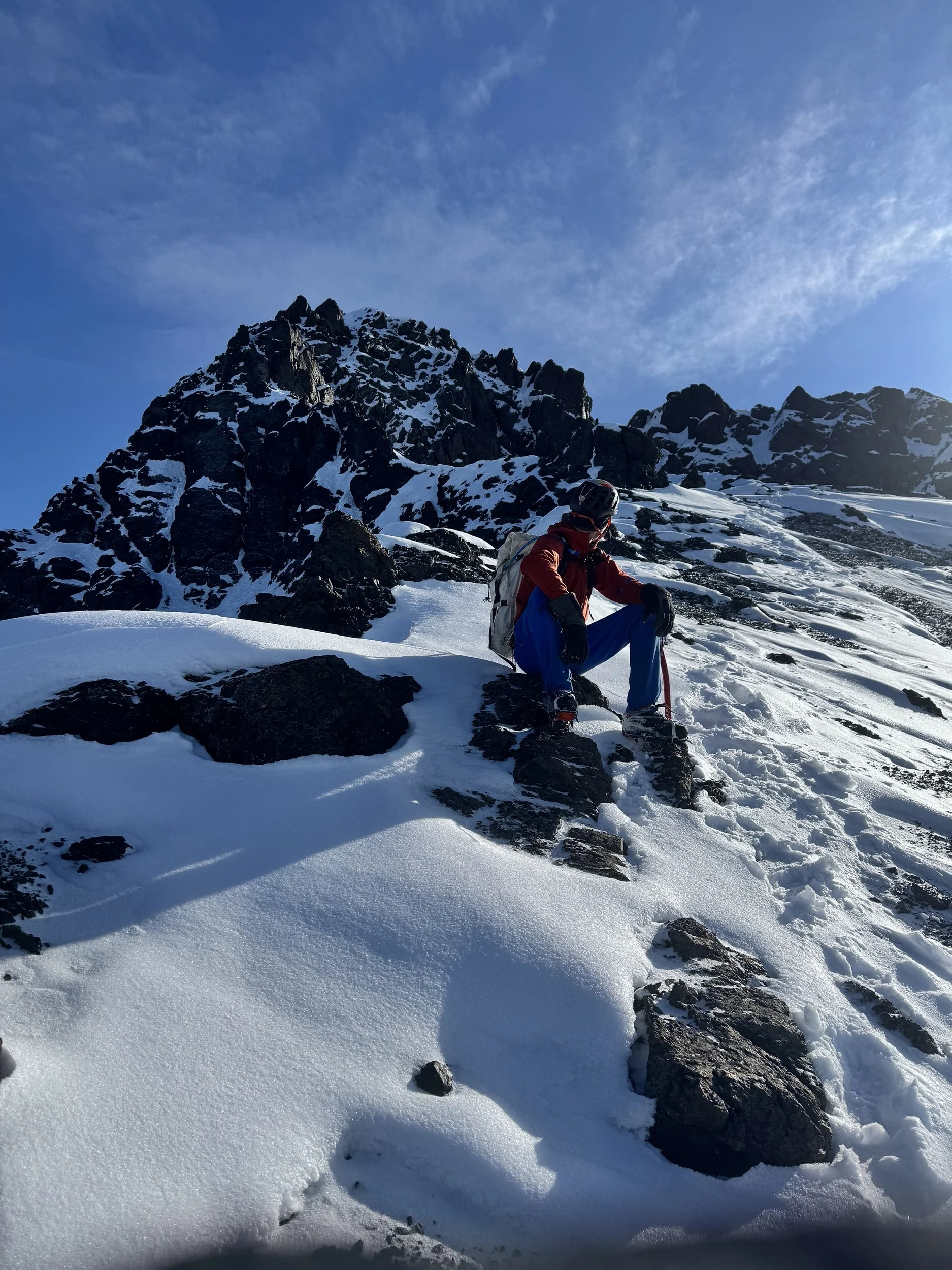 Male mountain climber sitting down looks up at the summit route.