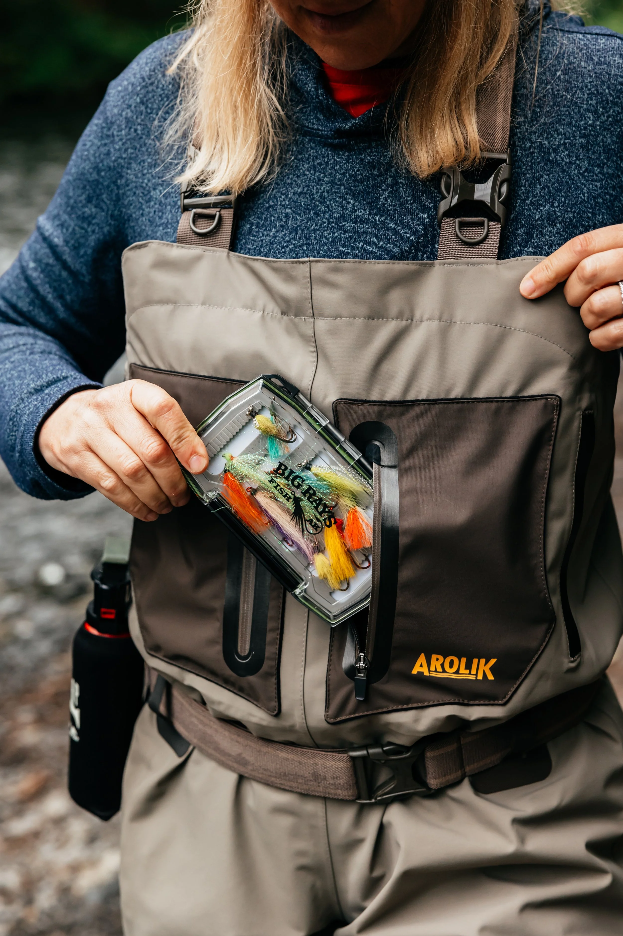Close-up of Arolik waders showing front storage pockets and fishing gear in use.