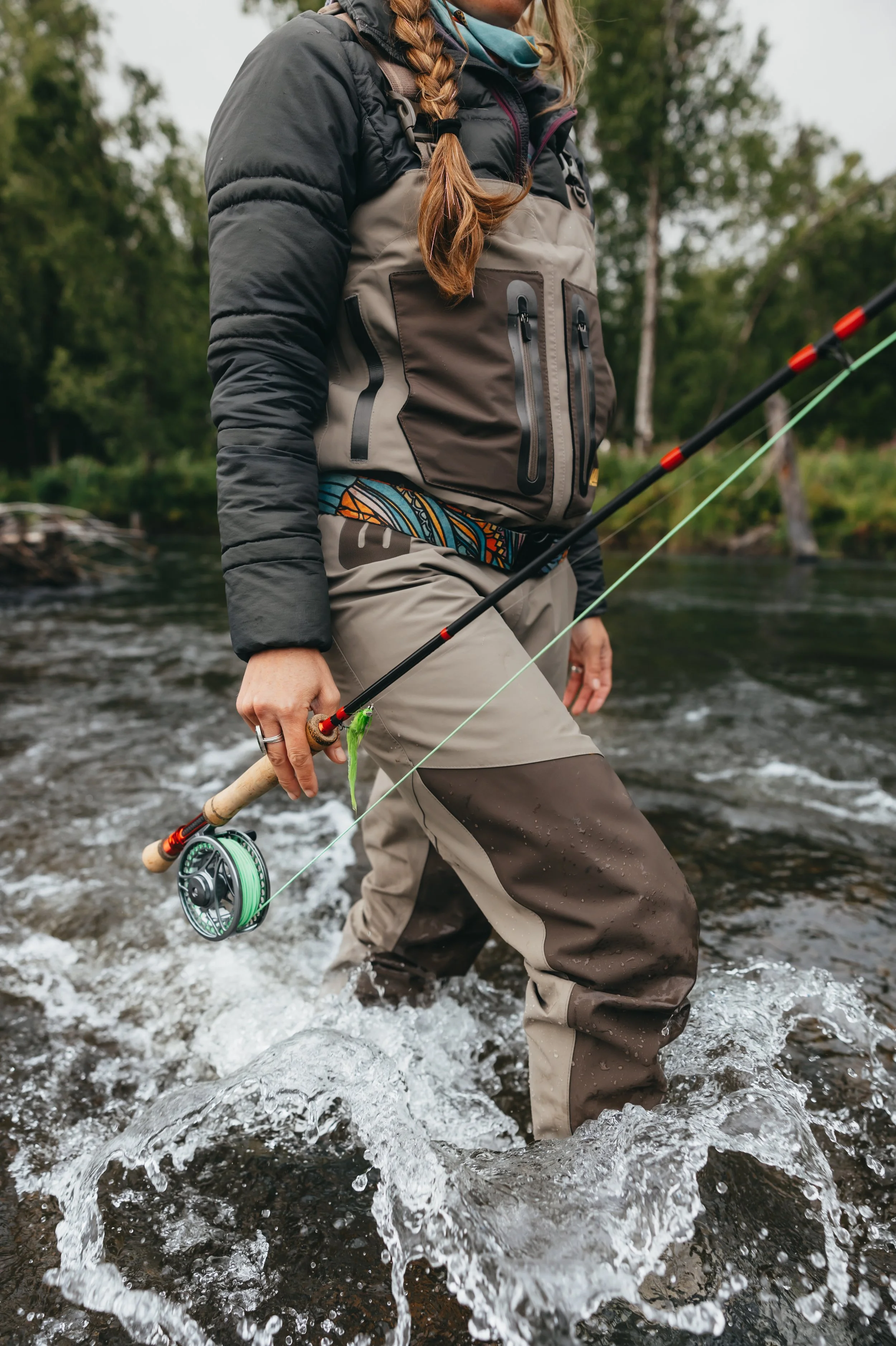 Close-up of Arolik fishing waders and fly rod in moving water, highlighting durable outdoor gear in action.