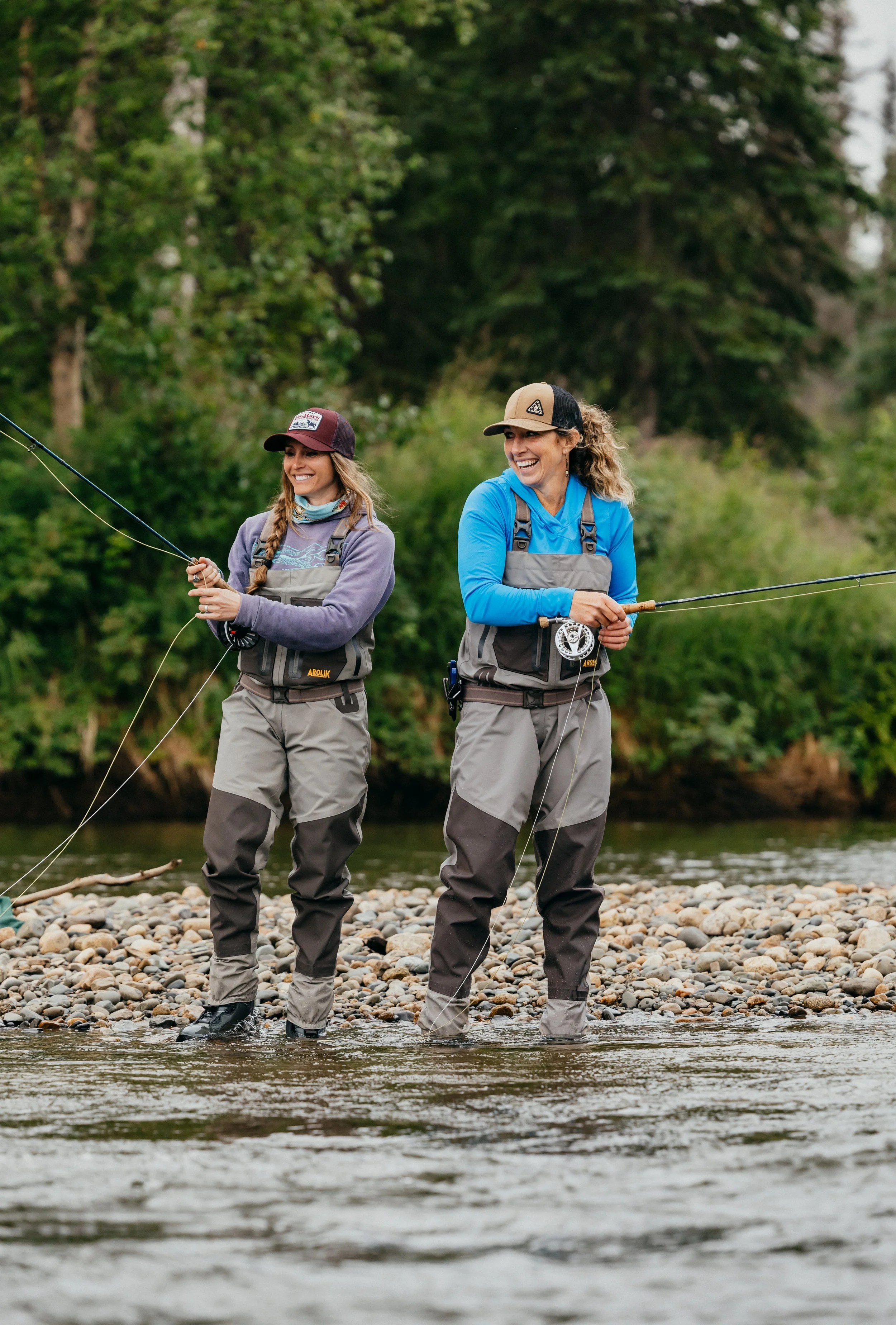 Two women fly fishing in Alaska wearing Arolik waders, casting lines side by side in a lifestyle outdoor scene.