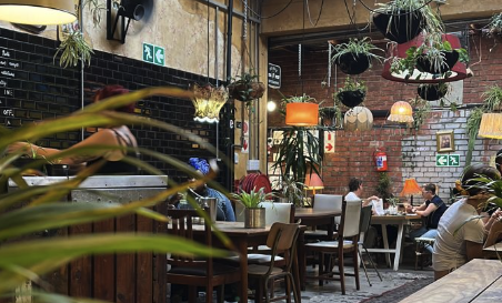 Interior of a cozy cafe with hanging plants, warm lighting, and people seated at tables.