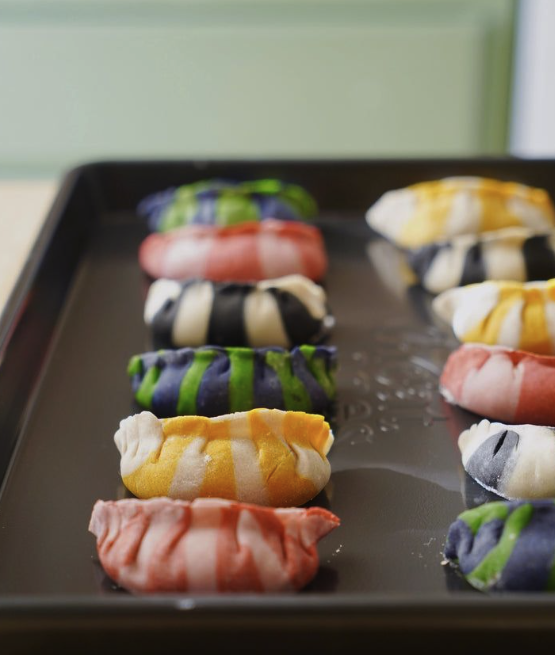 Colorful, striped cookies on a black baking sheet.