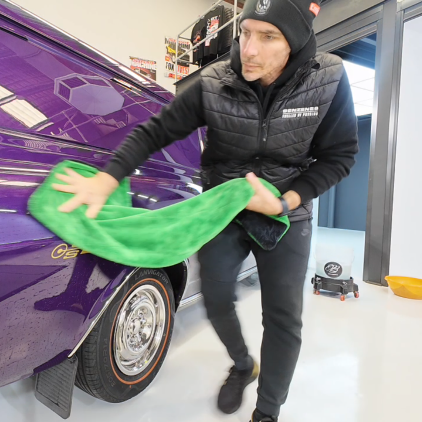 Man cleaning the purple vintage car with a green cloth in a garage or workshop.