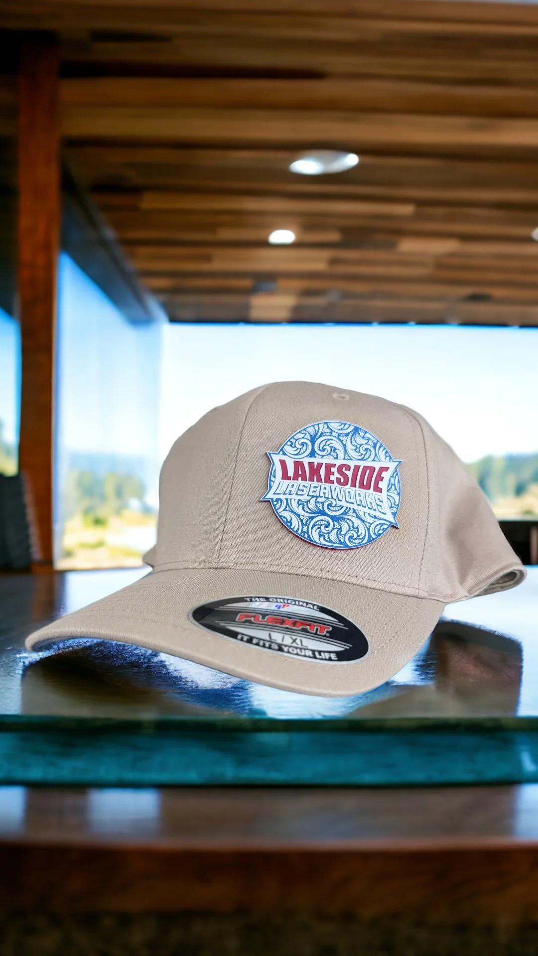 Beige cap with a Lakeside Laserworks logo on the front, placed on a reflective glass surface.