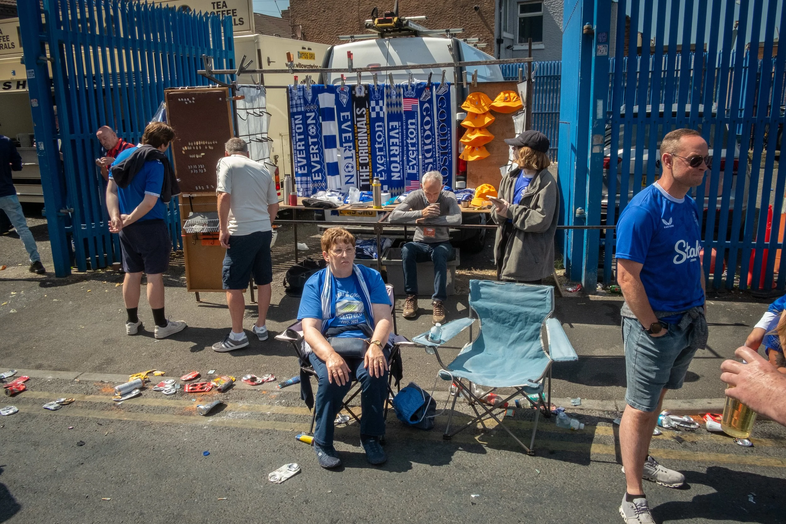 People gather outside a sports event concession stand with discarded cans and bottles on the ground.