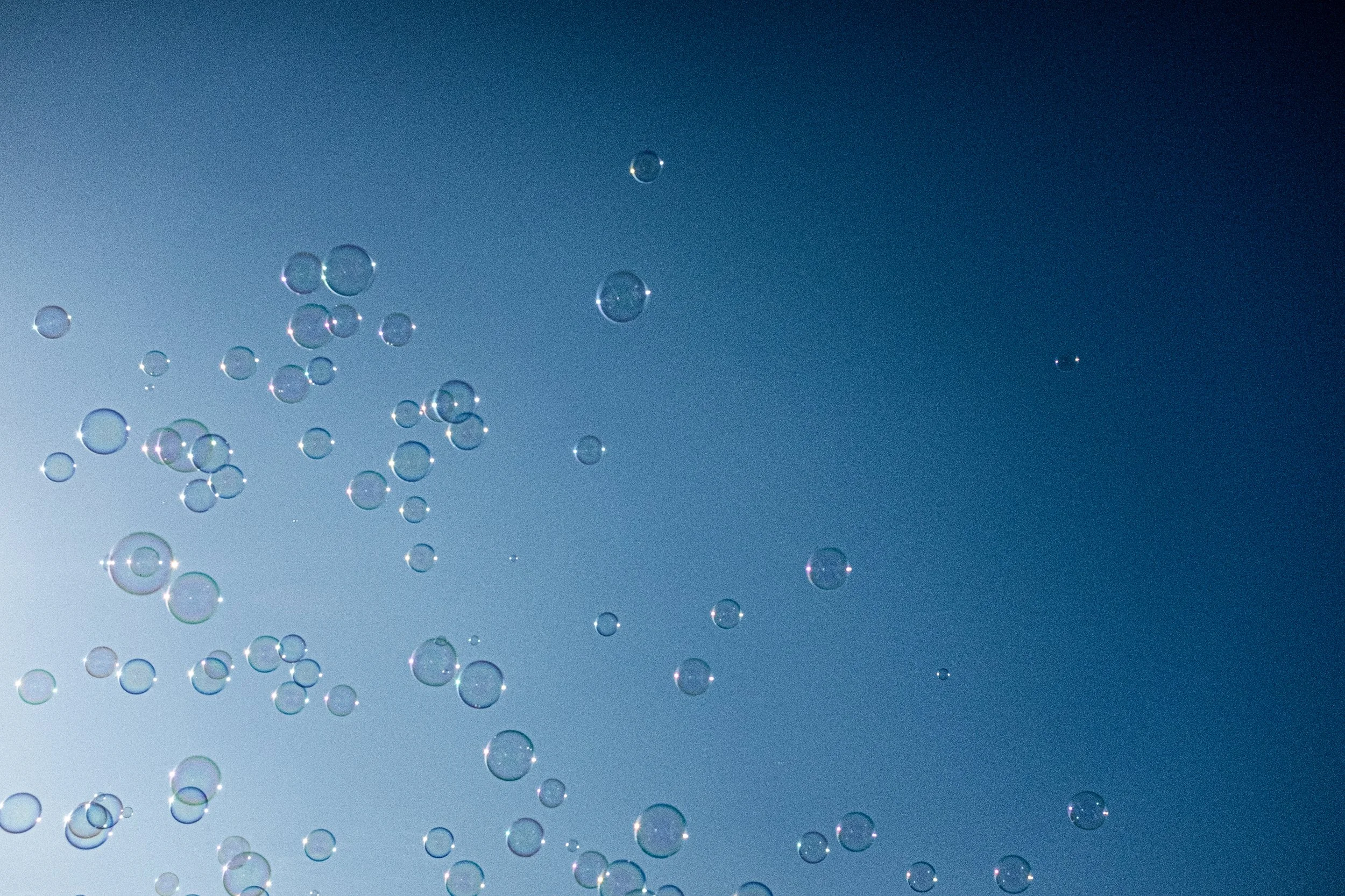 Multiple soap bubbles floating in the air against a clear blue sky.
