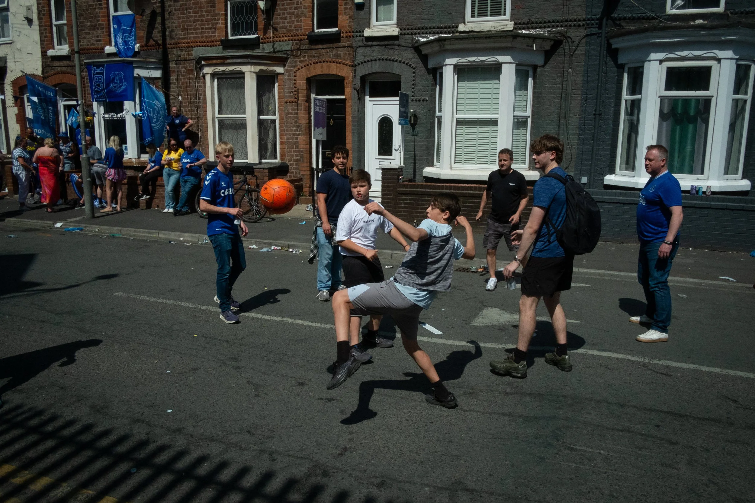 Group of children and a few adults playing street basketball during a street festival, with houses and onlookers in the background.