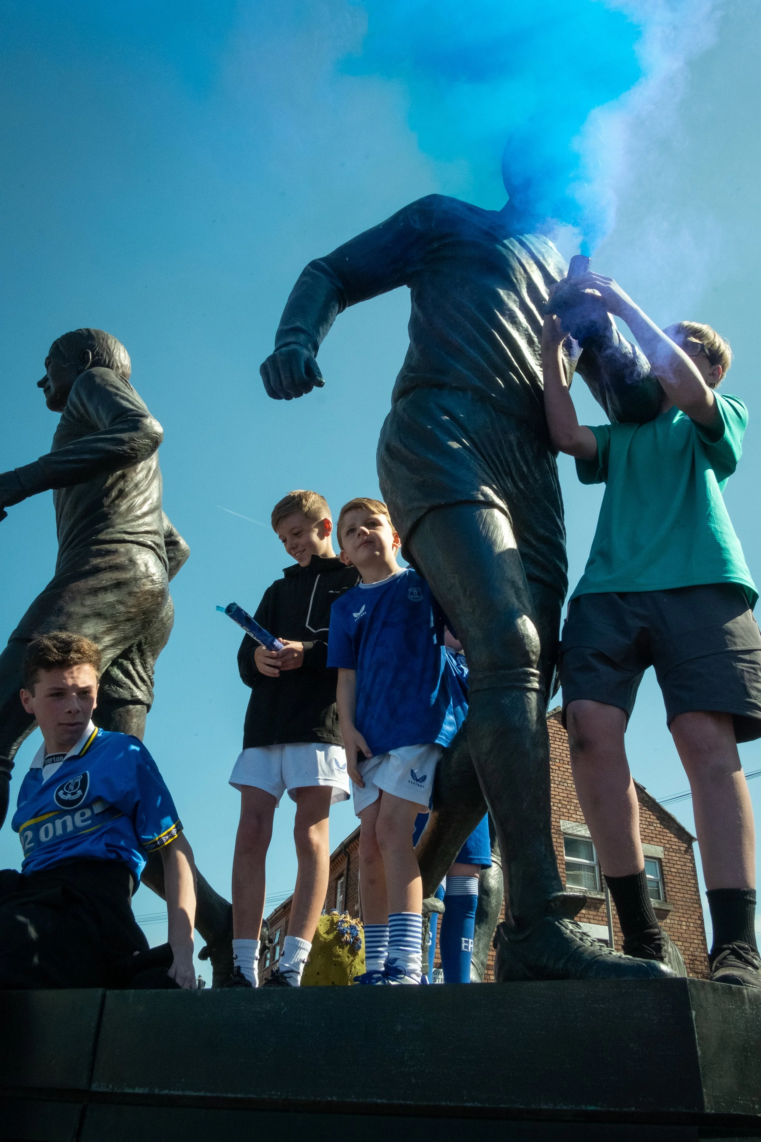 Children and a person in a teal shirt placing smoke bomb into a statue at a parade or celebration.