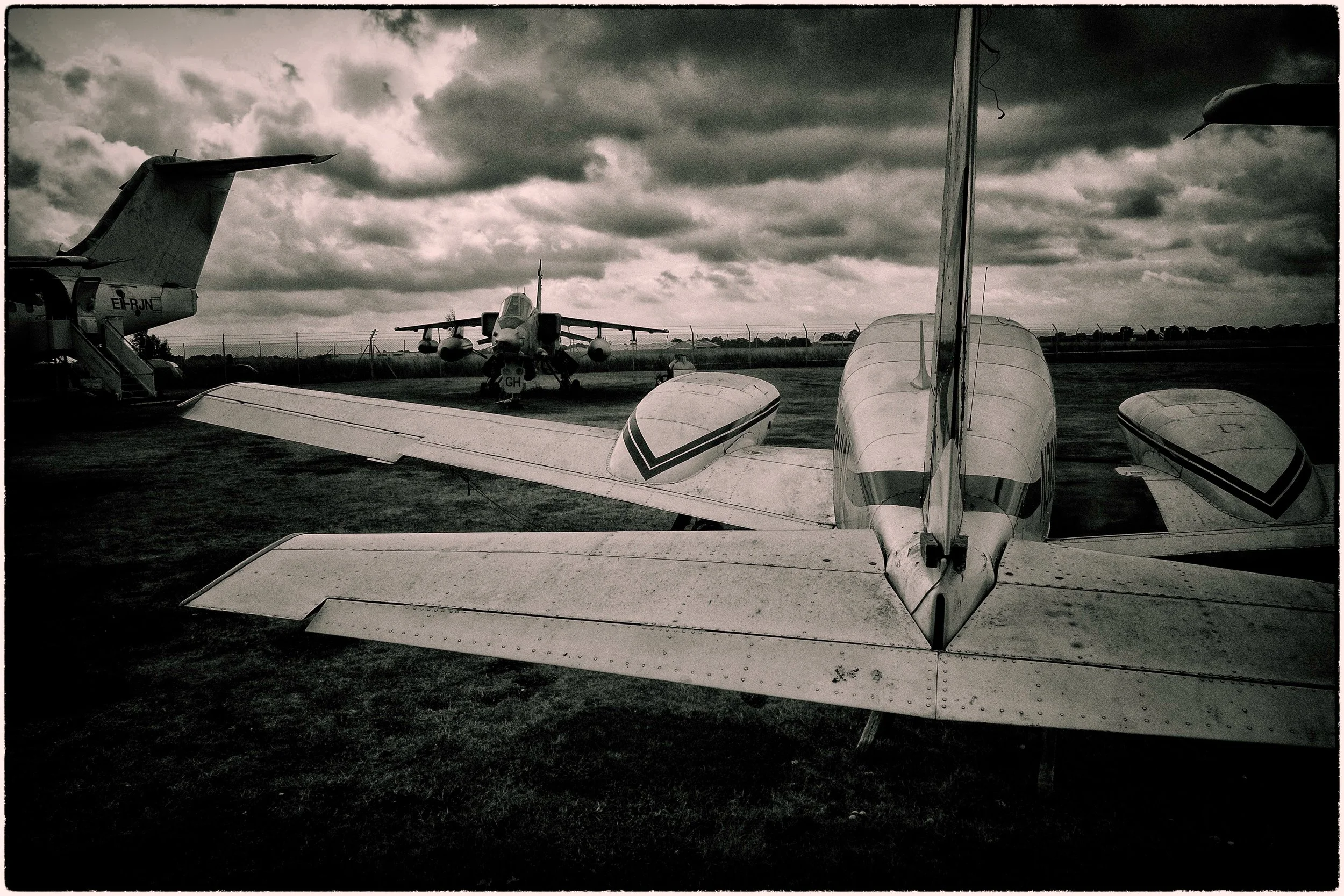 Several small airplanes parked on an airfield under a cloudy sky, with some aircraft visible from the rear, facing toward the horizon.