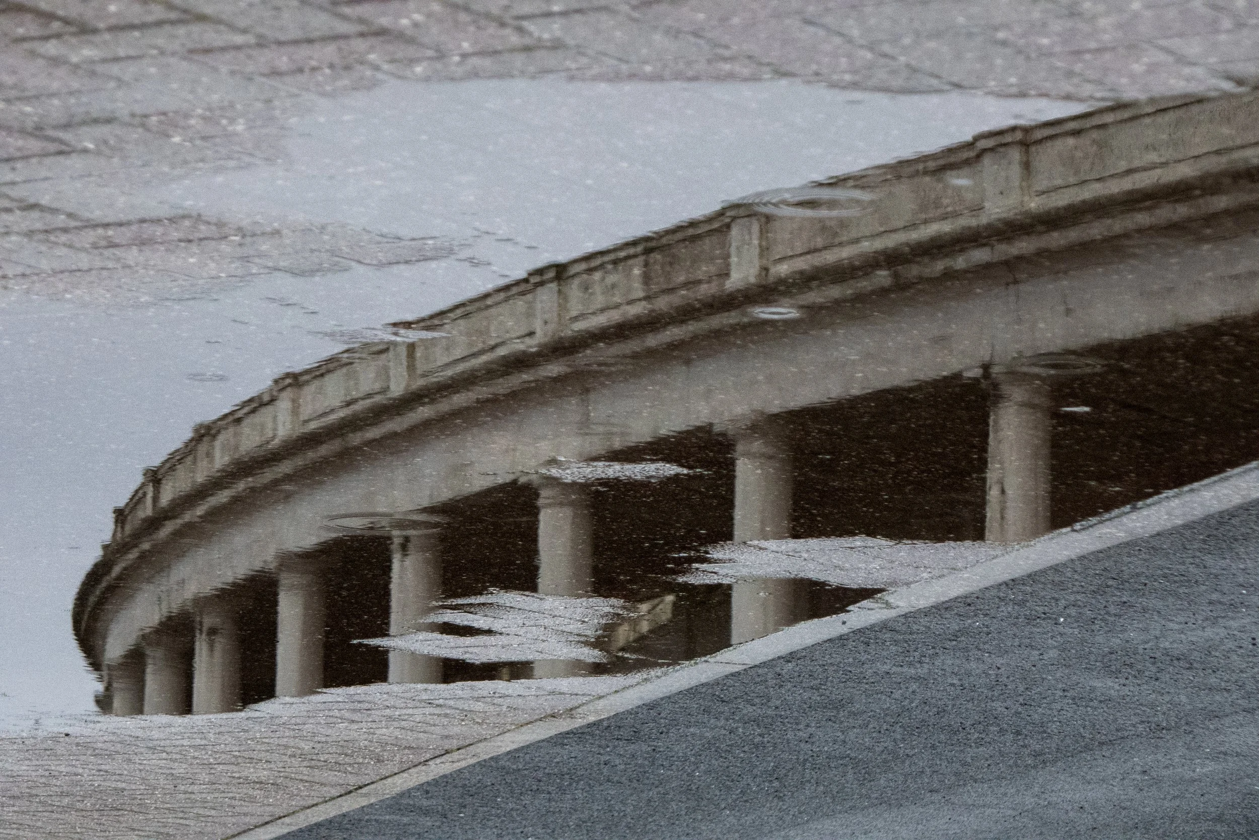 Reflection of a bridge with columns and a sidewalk in a puddle on the wet street