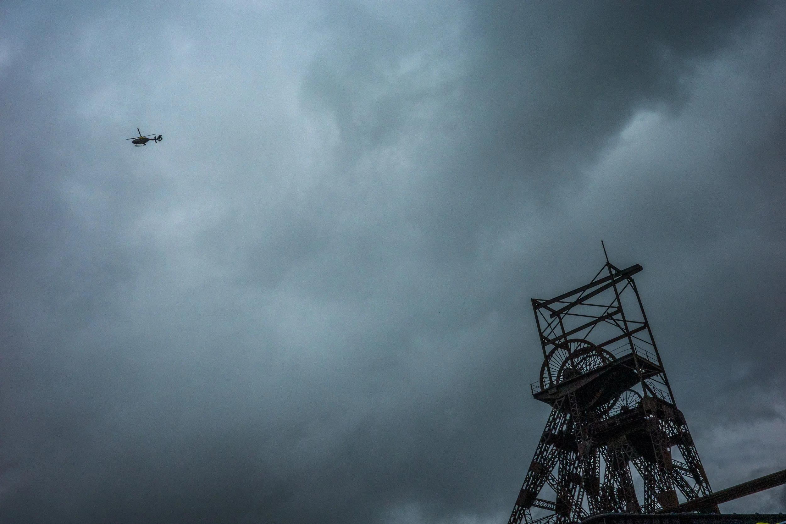 Dark stormy sky with a helicopter flying near a tall metal tower.