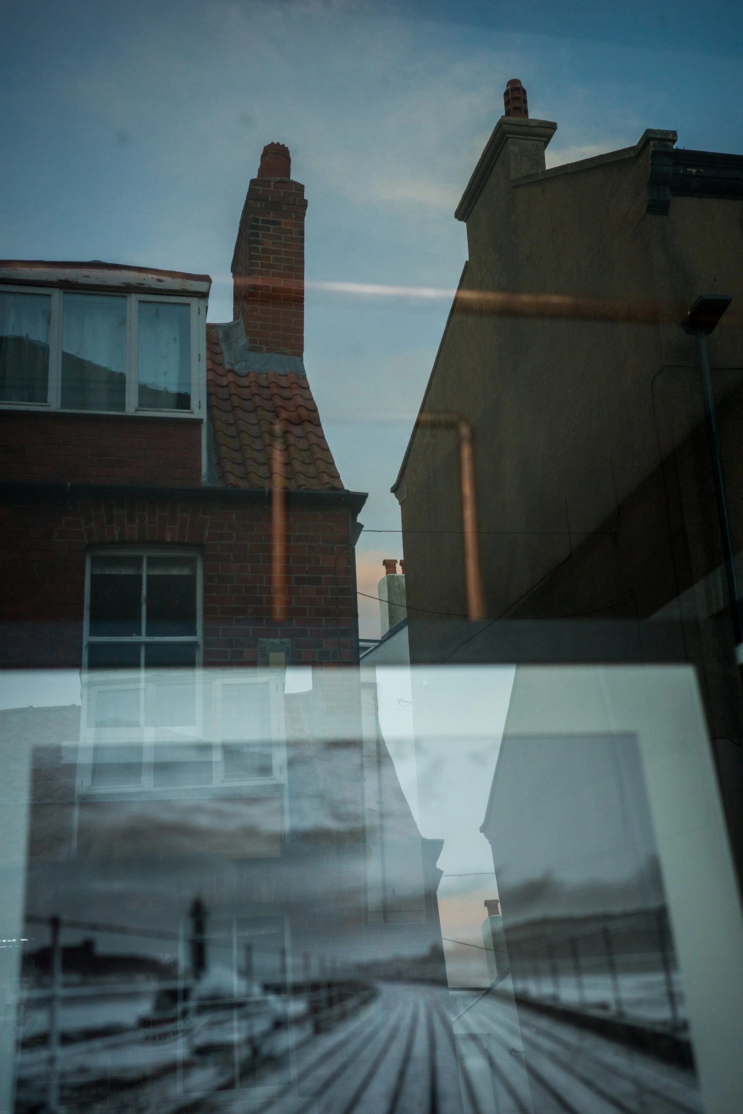 Reflection of buildings and boats on a glass window during dusk or dawn.