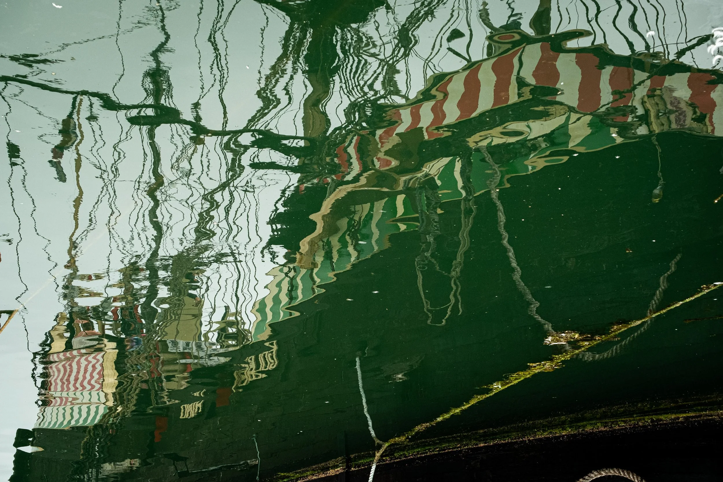Reflections of a building with striped awnings on the surface of a green boat