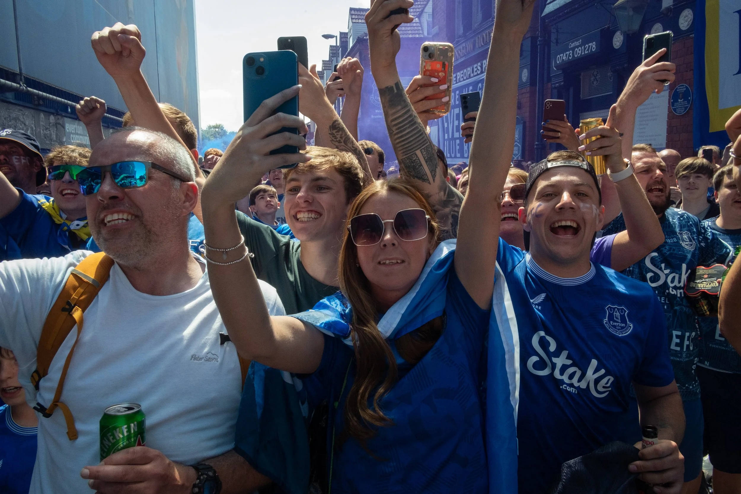 Crowd of happy sports fans, many wearing blue jerseys, taking selfies and celebrating outdoors.