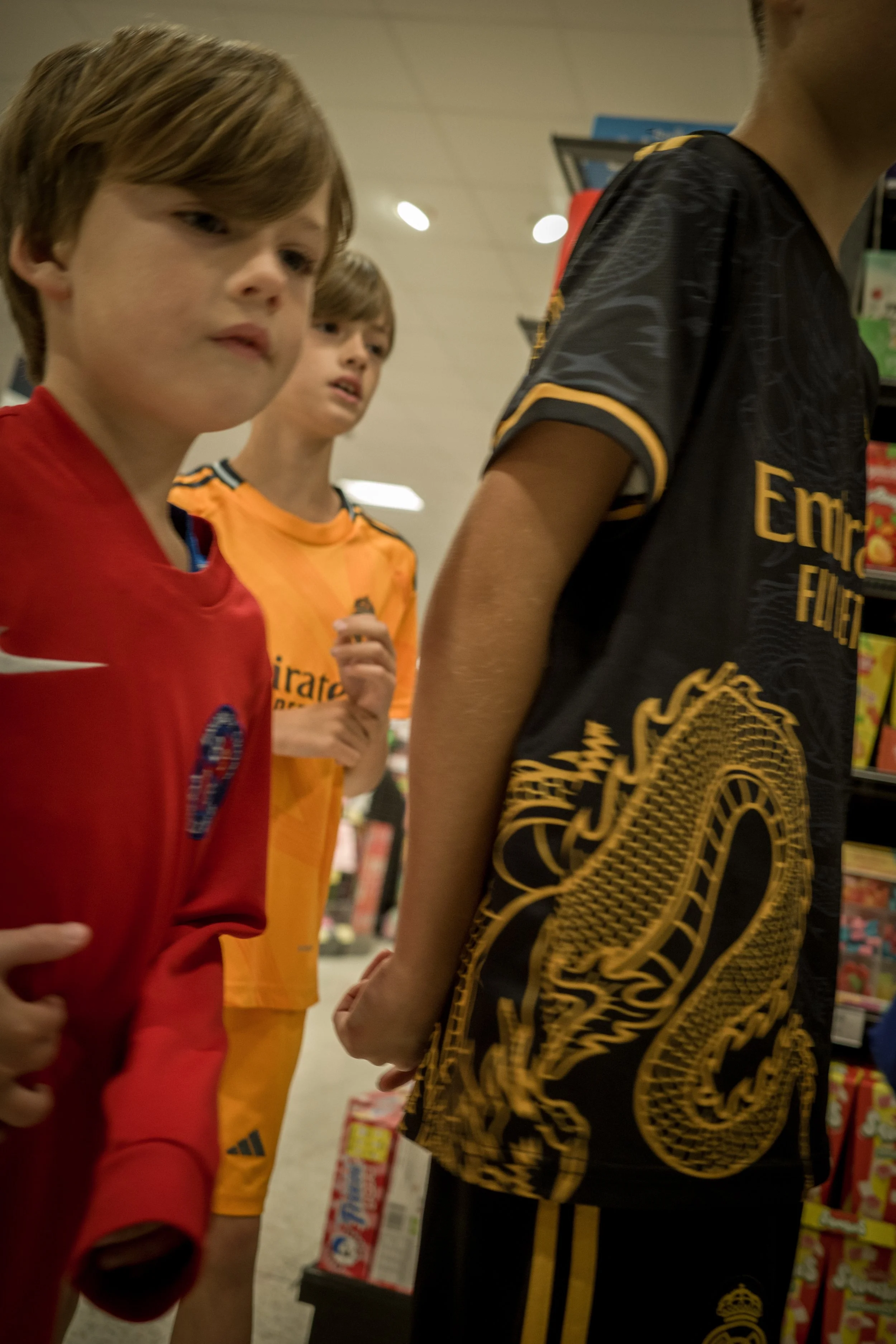 Three young boys in sports jerseys standing in a store aisle.