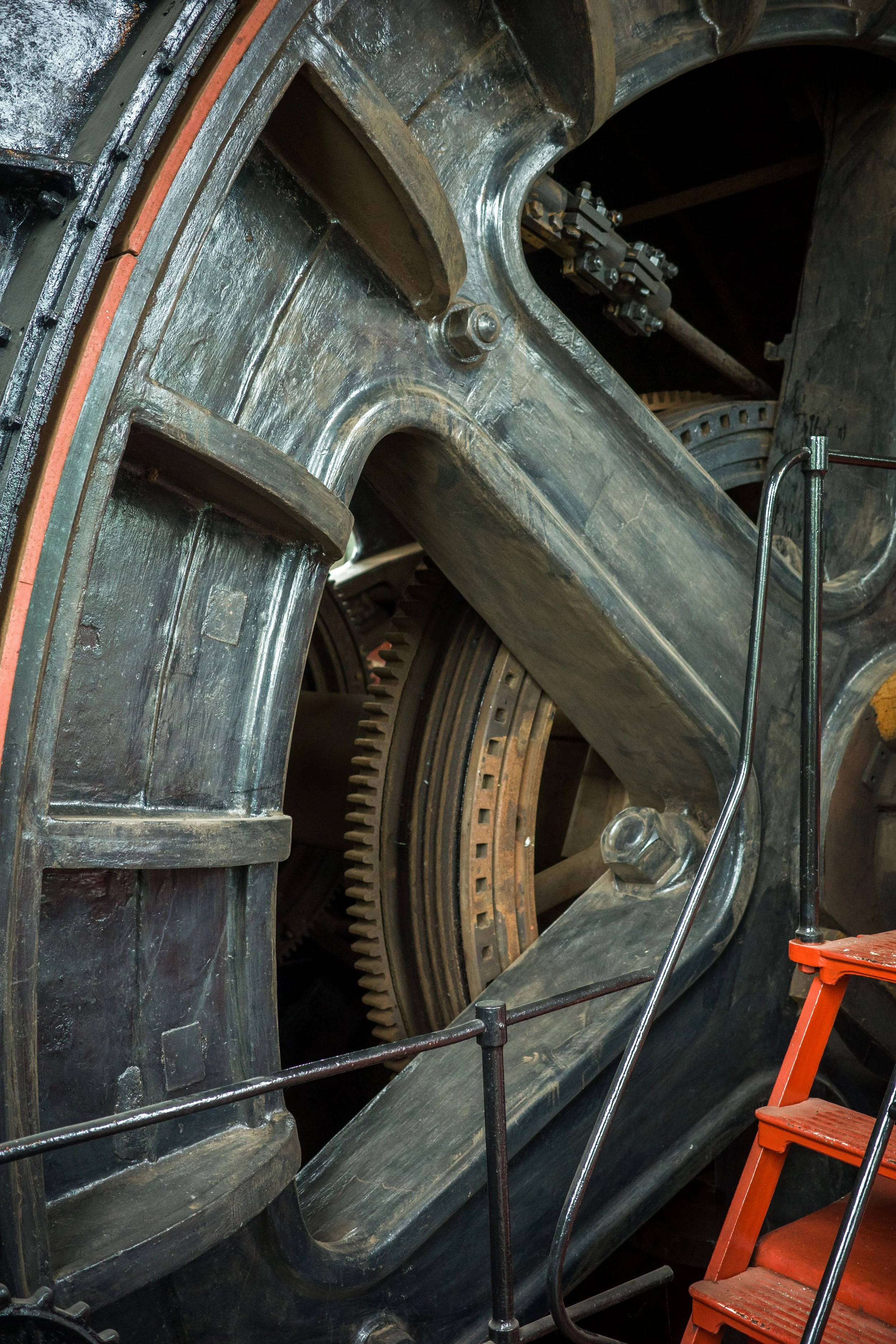 Close-up view of a large metallic gear and machinery inside an industrial or manufacturing setting, with a red step stool nearby.