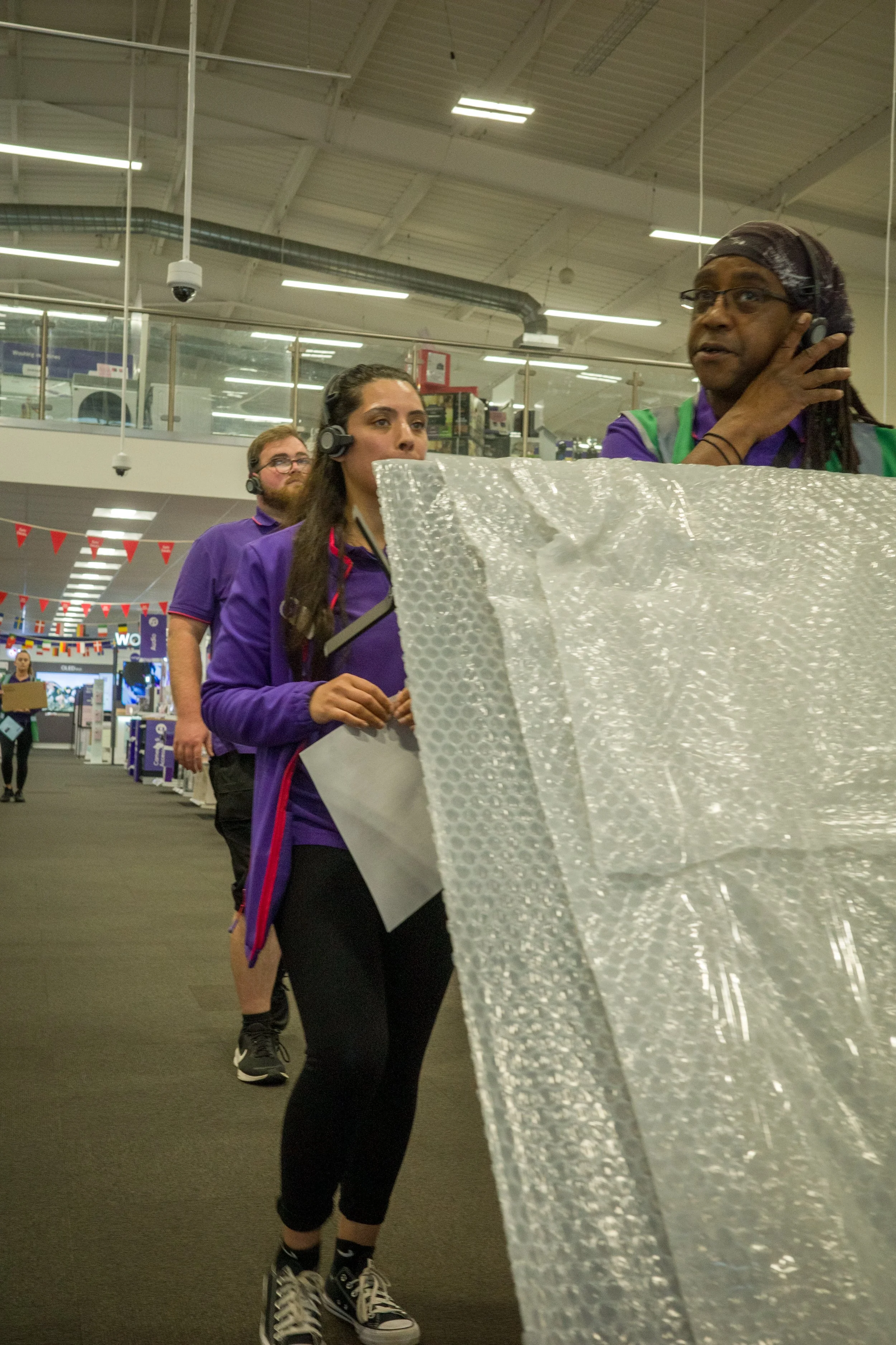Line of employees wearing purple uniforms working at a retail store, handling large sheets of bubble wrap.