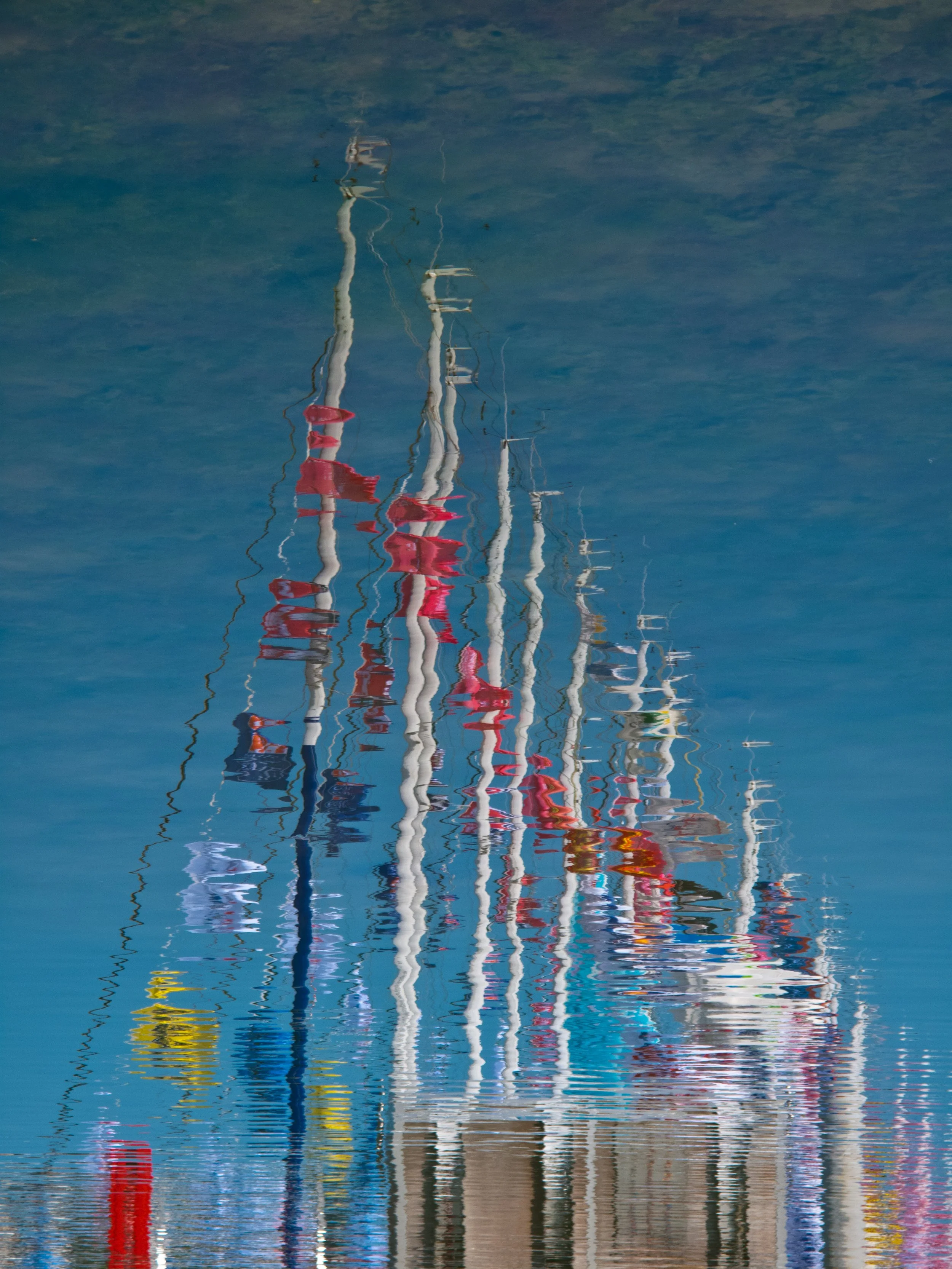Reflections of sailboats and their masts in water with ripples.