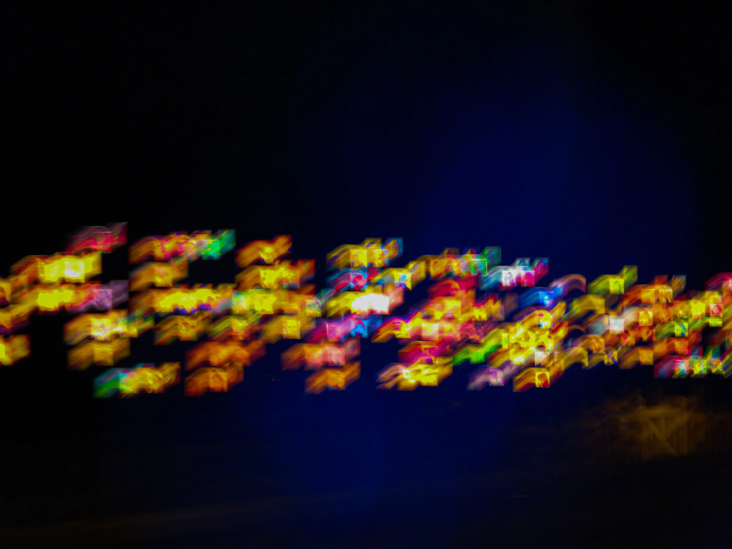 A night scene with colorful, blurred lights arranged horizontally against a dark background.